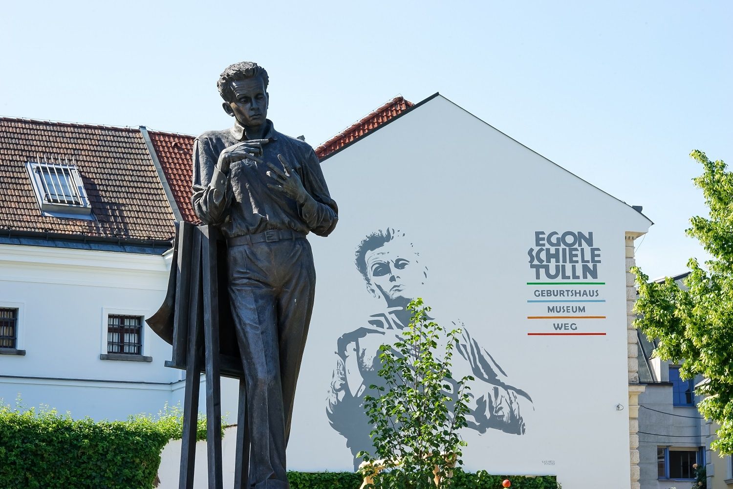 Socha Egona Schieleho pred budovou s nástennou maľbou a nápisom "Egon Schiele Tulln".