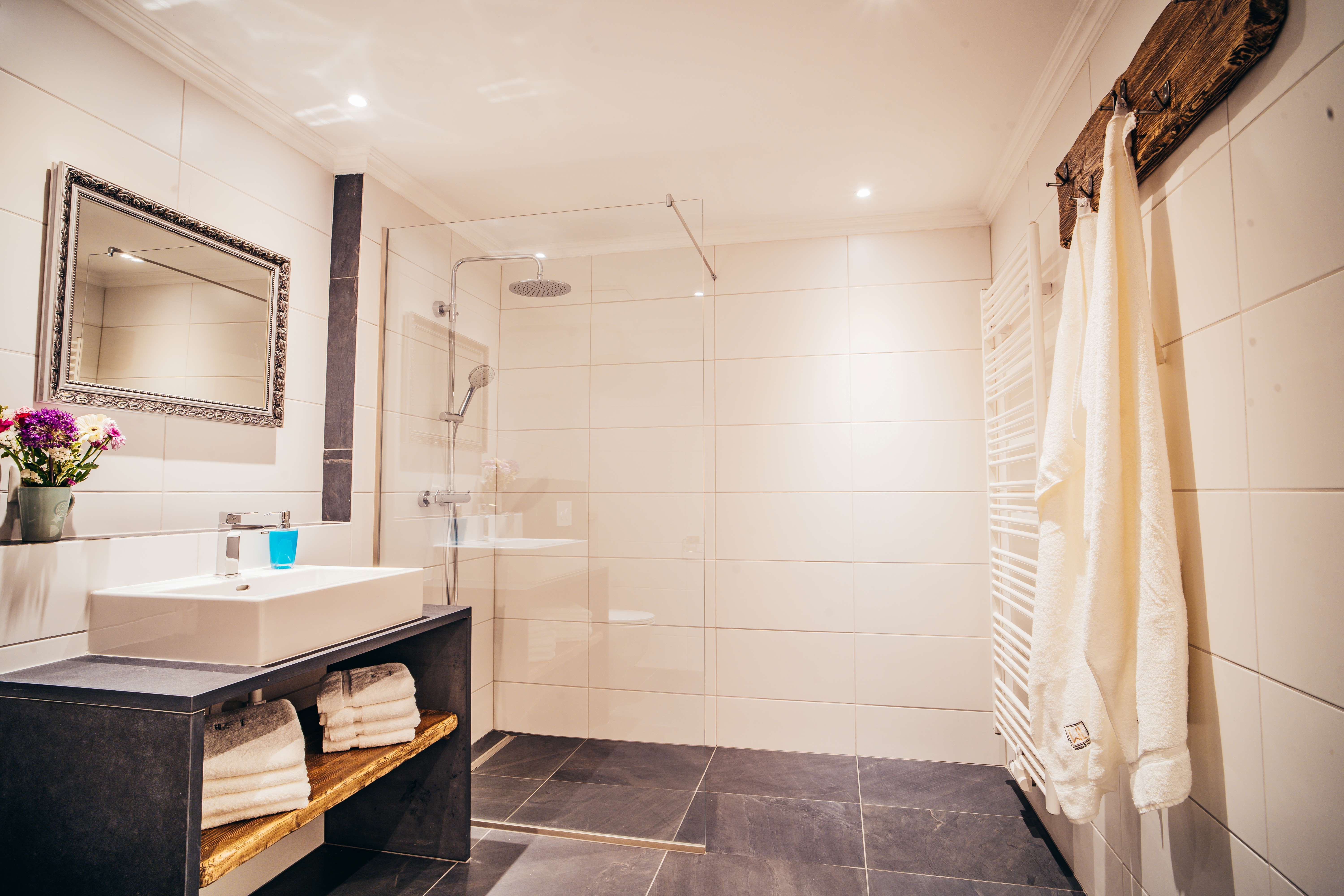 Moderná kúpeľňa s veľkým sprchovacím kútom, umývadlom, zrkadlom a uterákmi.