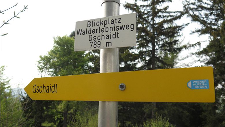 Smerovník k vyhliadkovému miestu lesného zážitkového chodníka Gschaidt, 789 m, so žltou značkou a logom Viedenských Alp.