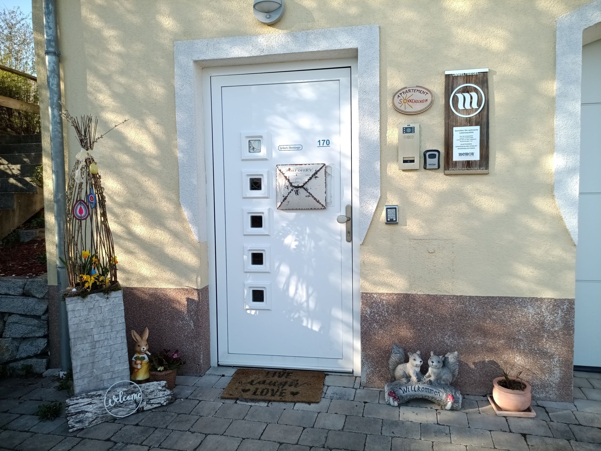 Vstupná časť domu s dekoratívnymi prvkami, ako je zajac, uvítací nápis a kvety.