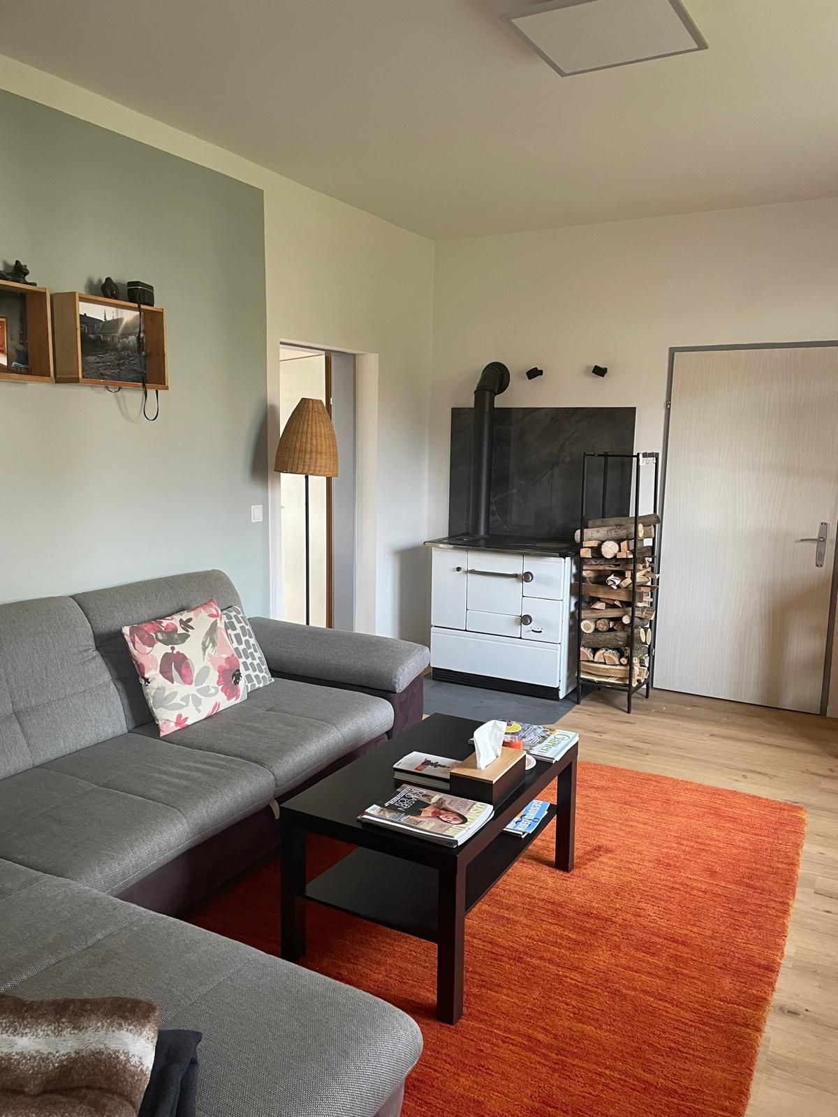 Útulná obývacia izba so sivou pohovkou, konferenčným stolíkom, červeným kobercom a krbovými kachľami.