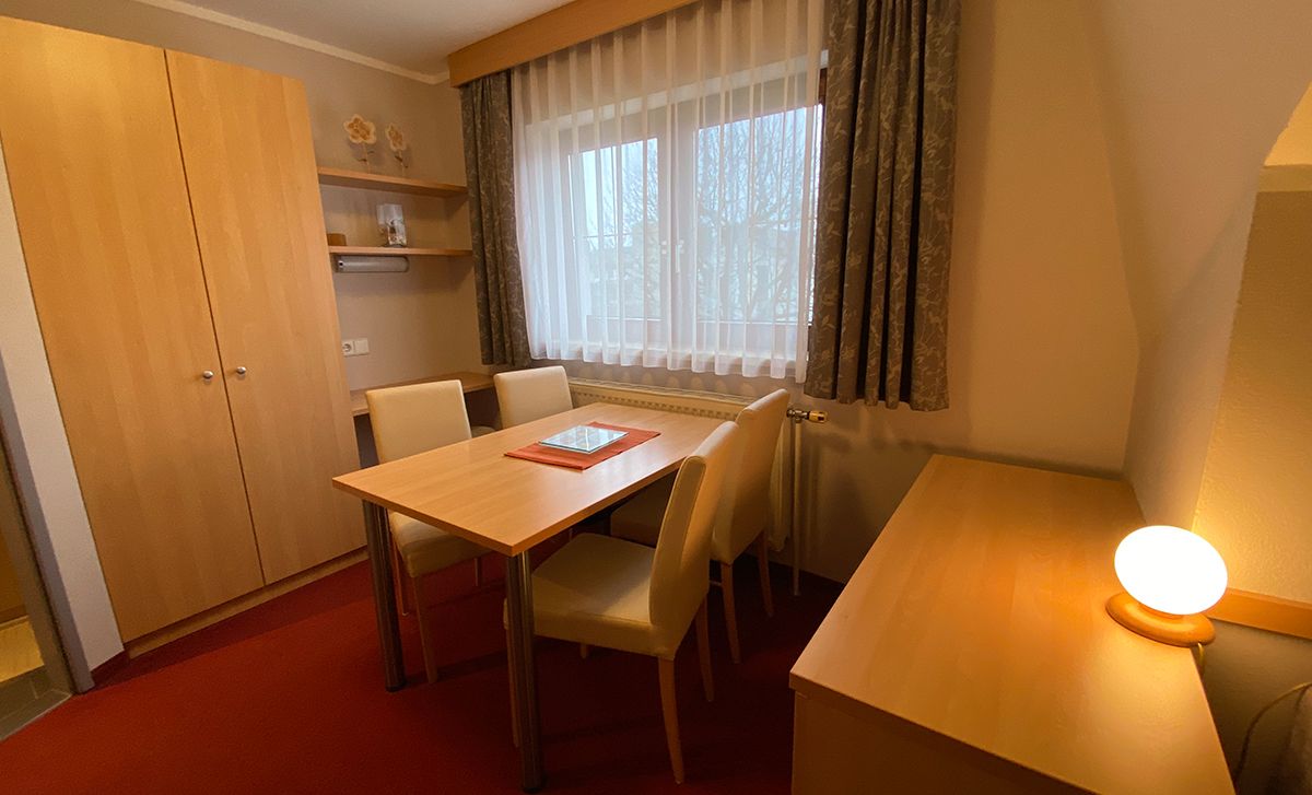 Útulná izba s dreveným nábytkom, stolom, stoličkami a oknom so závesmi.