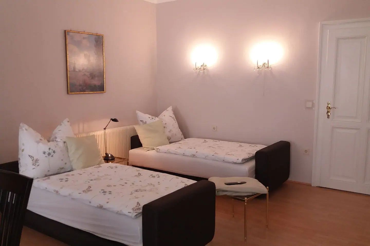 Dve samostatné postele v svetlej izbe s nástennými lampami a obrazom na stene.