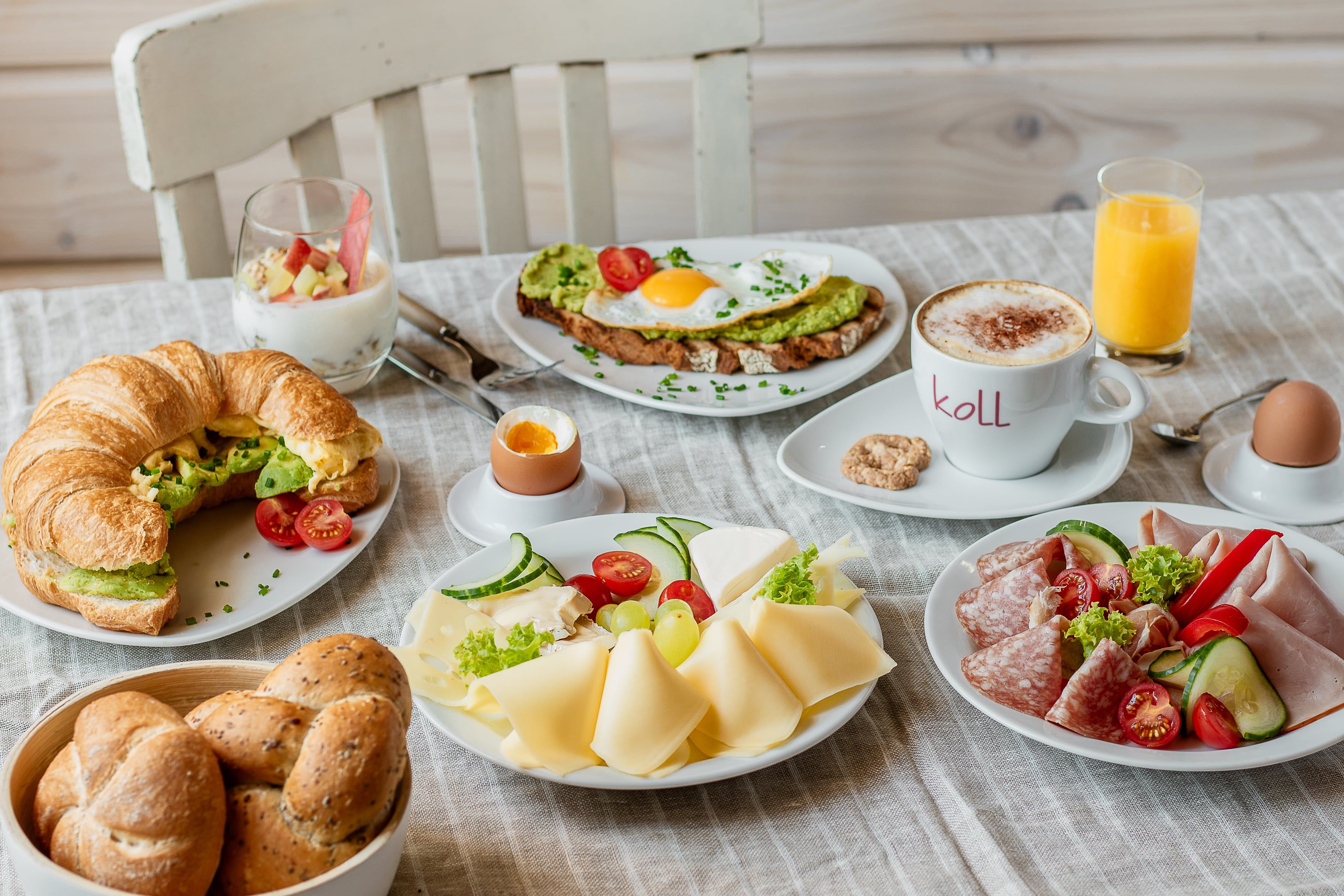 Bohaté raňajky s croissantom, chlebom, syrom, údeninami, vajíčkom, jogurtom, kávou a pomarančovým džúsom na stole.