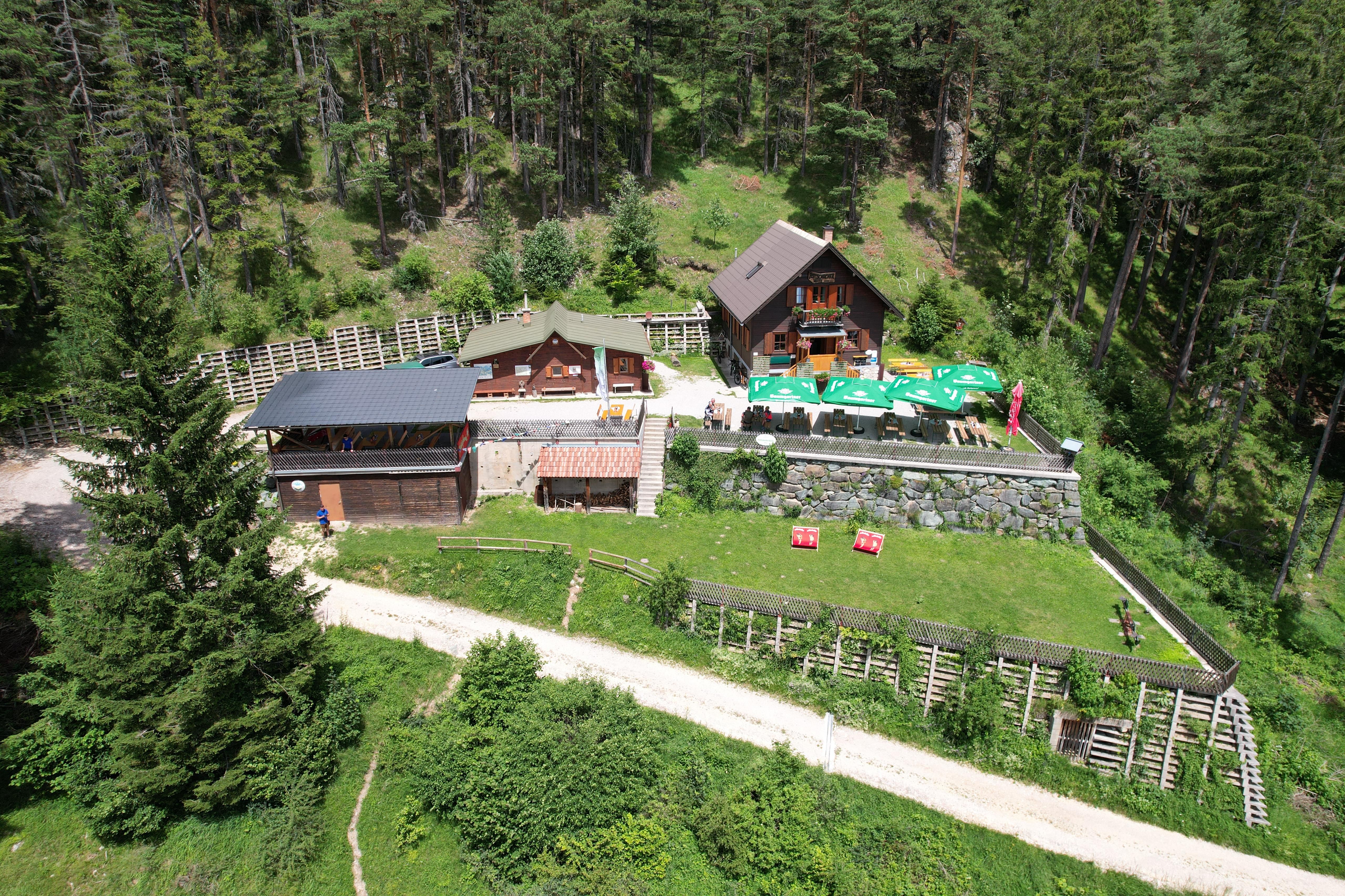 Letecký pohľad na chatu Potschacherhütte v zalesnenej oblasti s okolitými stromami a terasou so slnečníkmi.