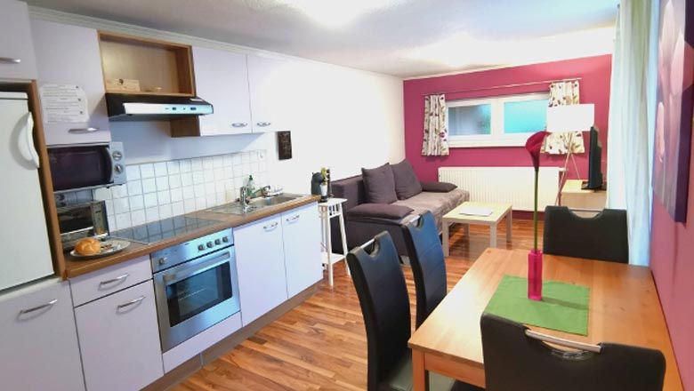 Pohľad do interiéru moderného bytu s kuchyňou, jedálenským stolom a pohovkou.