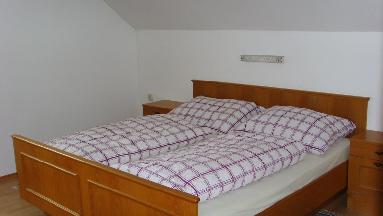 Sp&aacute;lňa s drevenou posteľou a &scaron;achovnicov&yacute;mi posteľn&yacute;mi obliečkami.