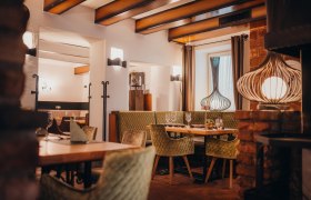 Útulná reštaurácia s drevenými trámami, zelenými čalúnenými stoličkami a ozdobnými lampami.