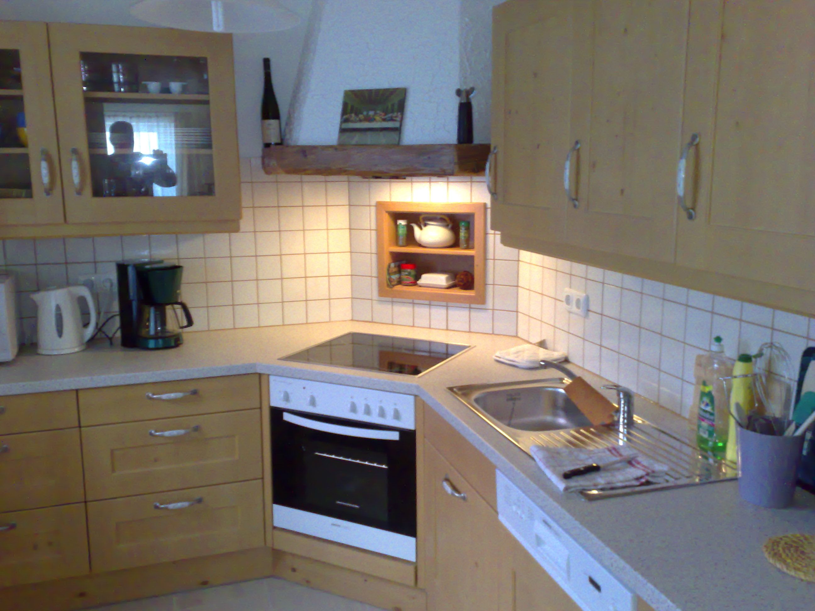 Kuchyňa s drevenými skrinkami, sporákom, drezom a kávovarom.