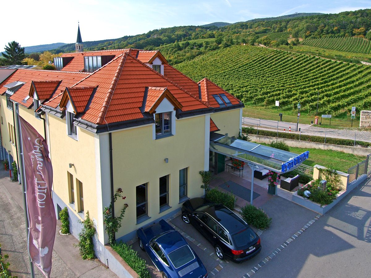 Exteriérový pohľad na hotel Turmhof s červenými strechami a okolitými vinicami.