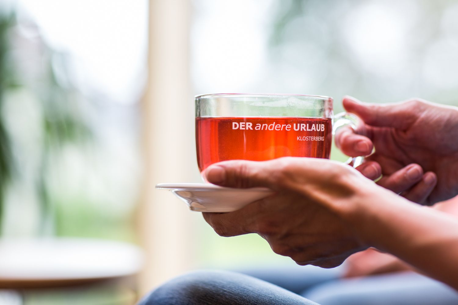 Detailný záber na ruky držiace pohár s červeným nápojom s nápisom "DER andere URLAUB KLOSTERBERG".
