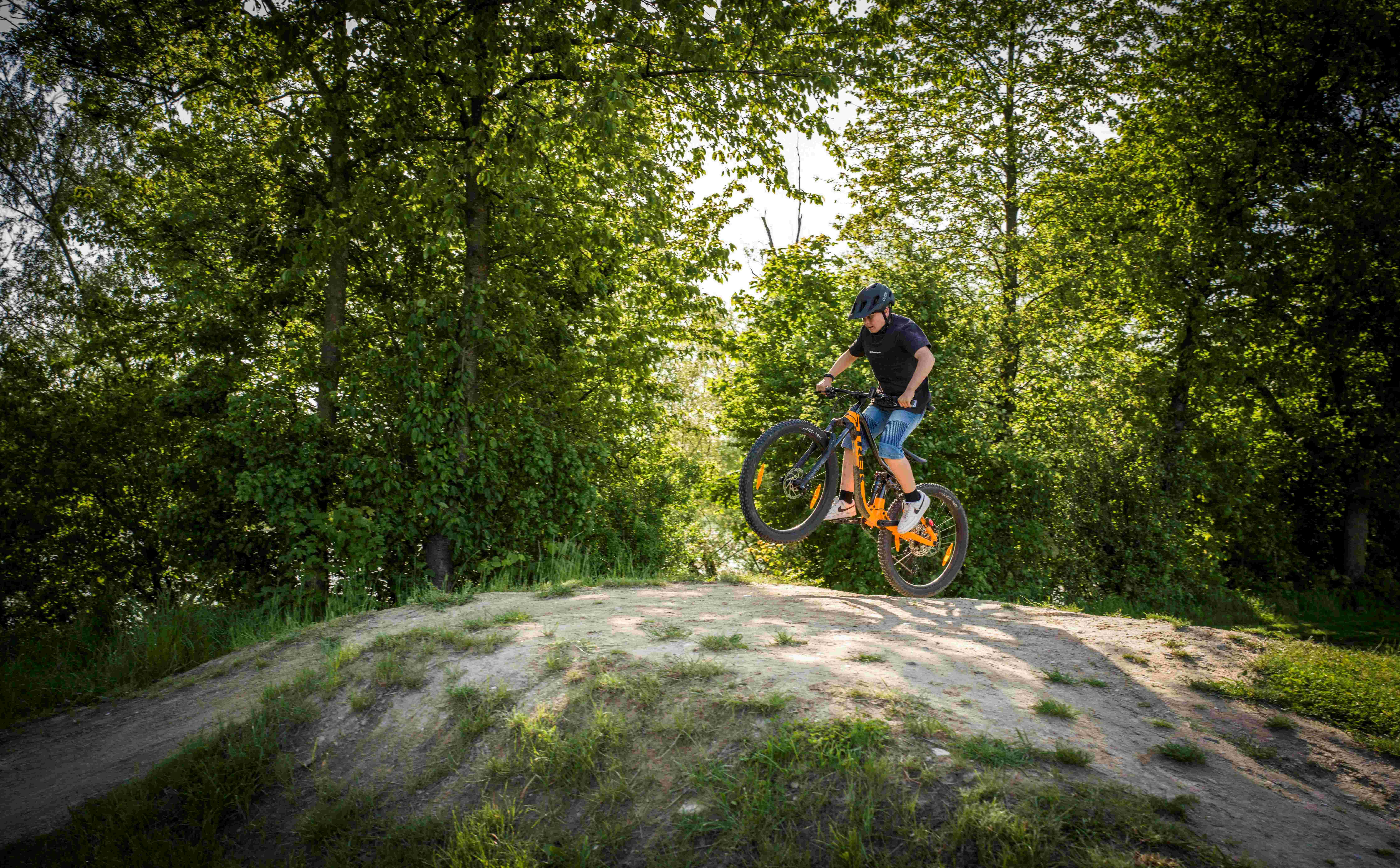 Cyklista na horskom bicykli skáče cez kopec v zalesnenej oblasti.
