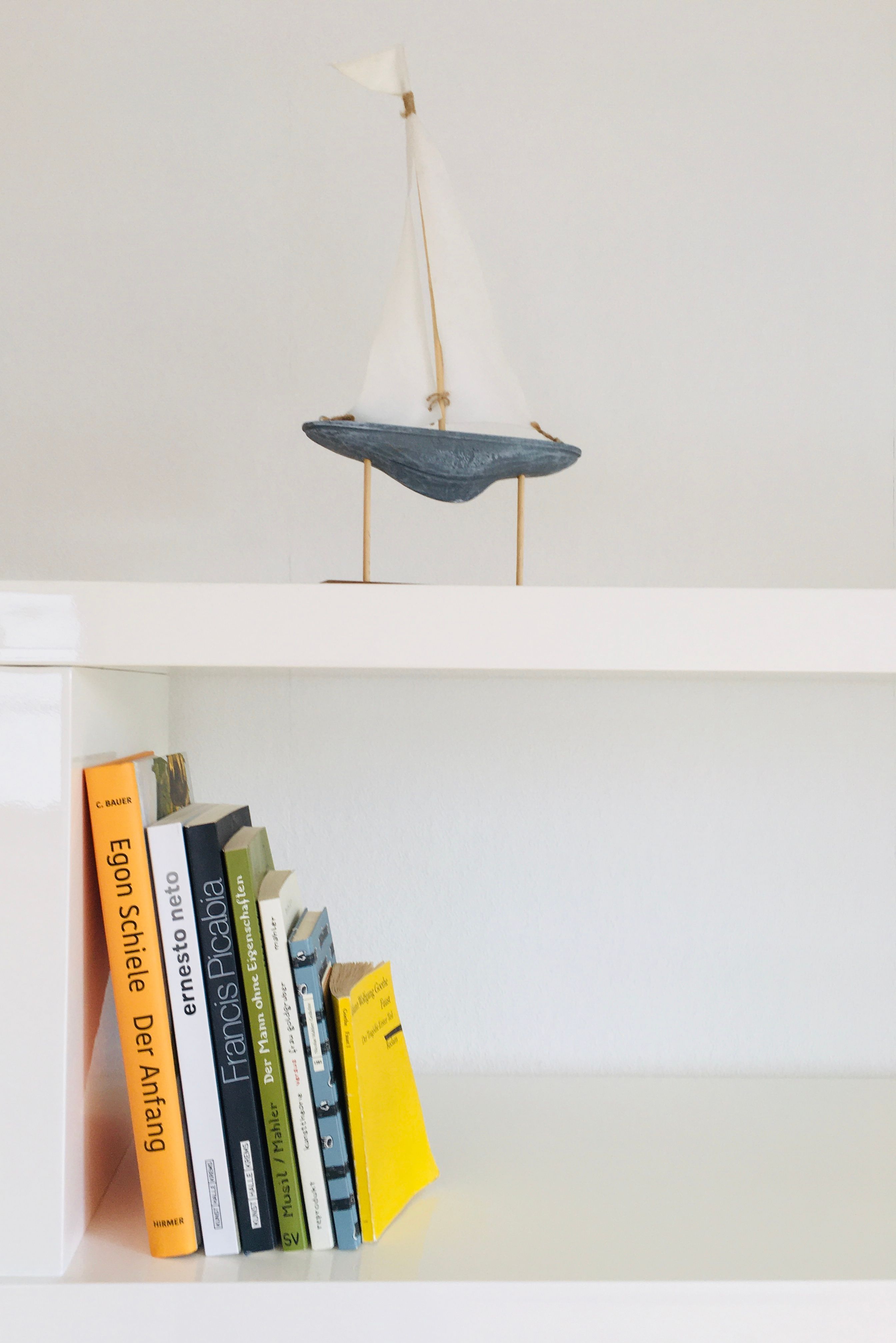 Biela polica s knihami a malou plachetnicou ako dekoráciou.