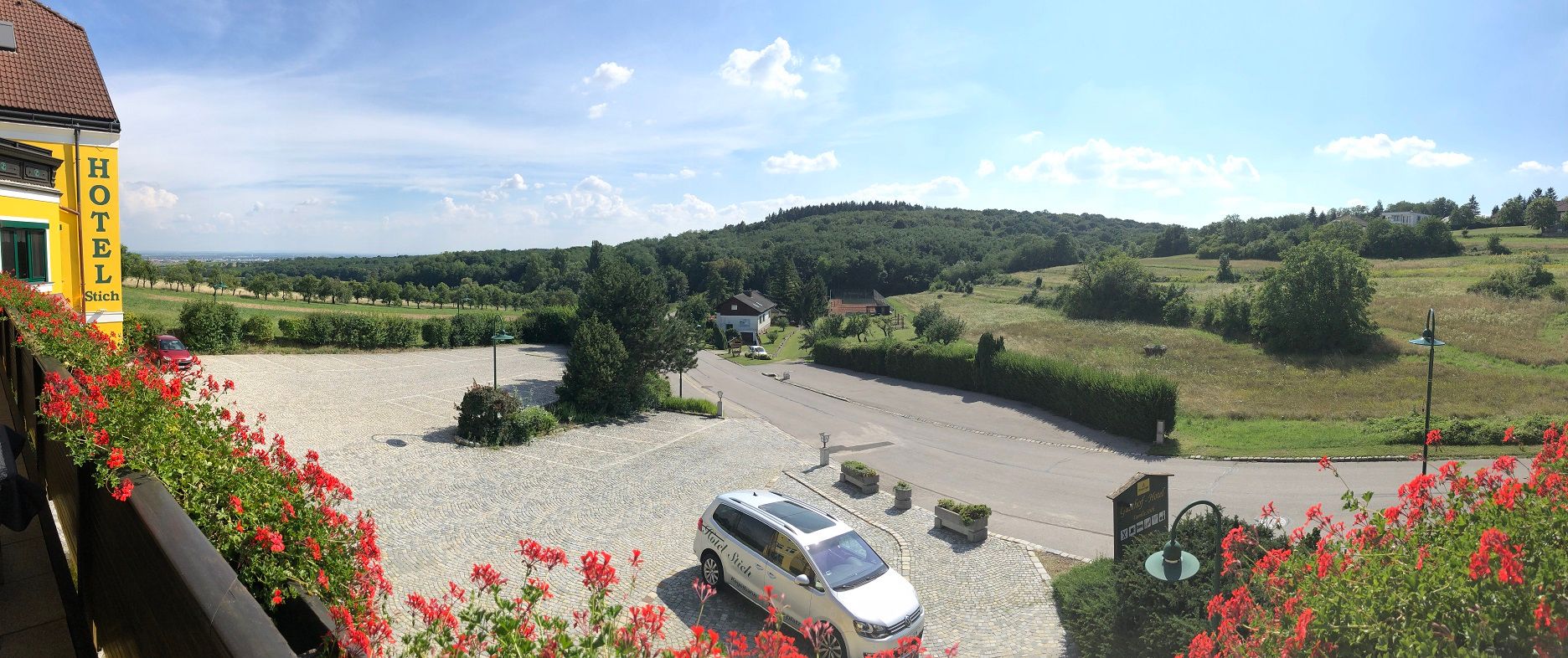 Panoramatický pohľad na vidiecku krajinu s kopcami a lúkami z hotelového balkóna.