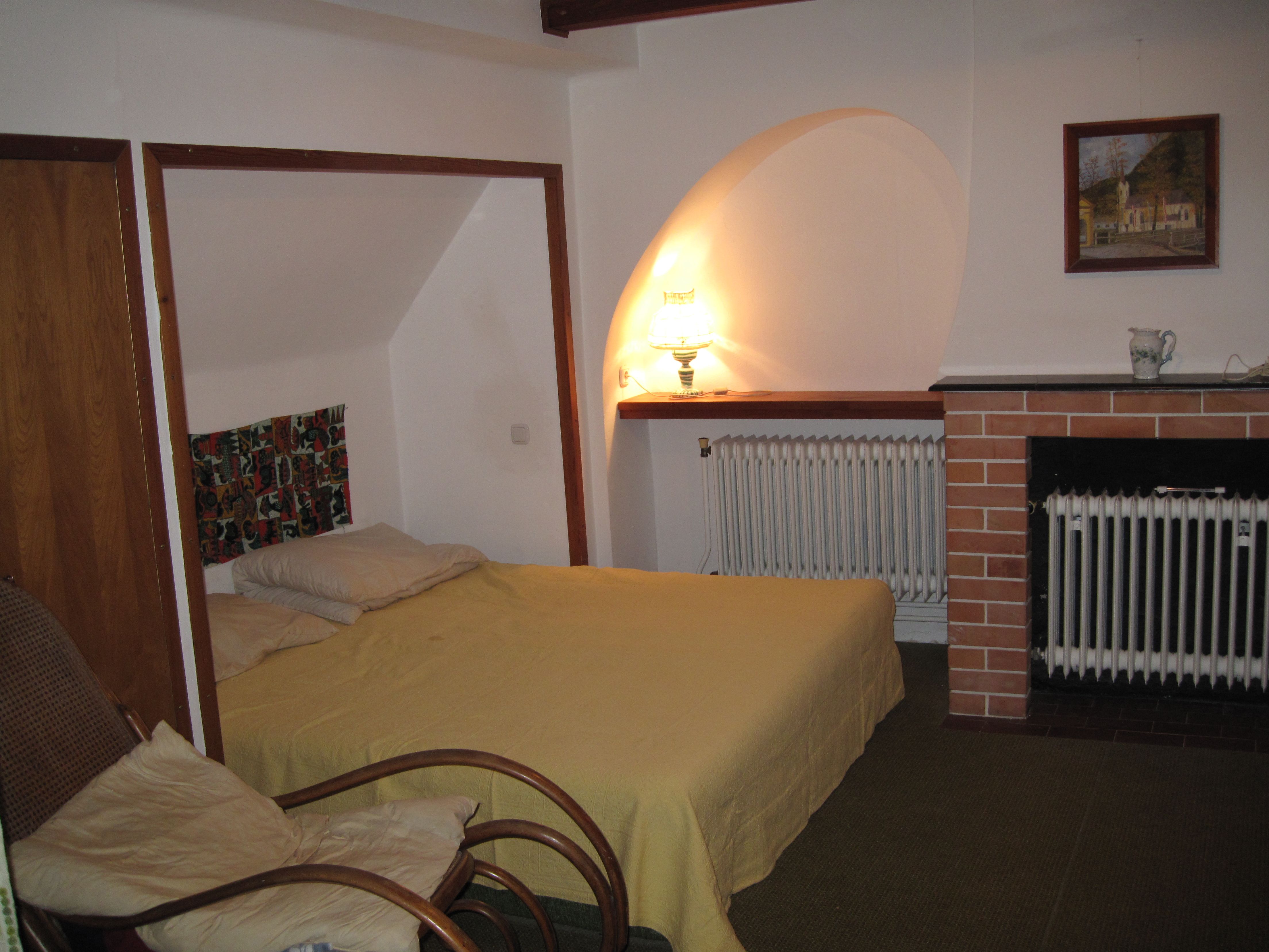 Útulná spálňa s posteľou, kreslom, lampou a krbom.