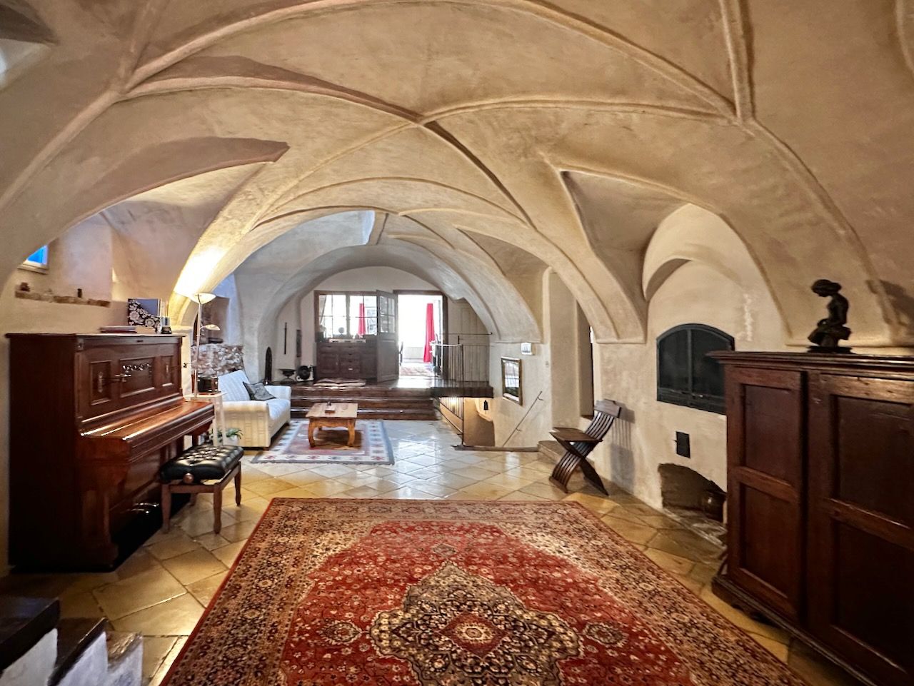 Historická prijímacia hala s klenutým stropom, kobercom, klavírom a dreveným nábytkom.