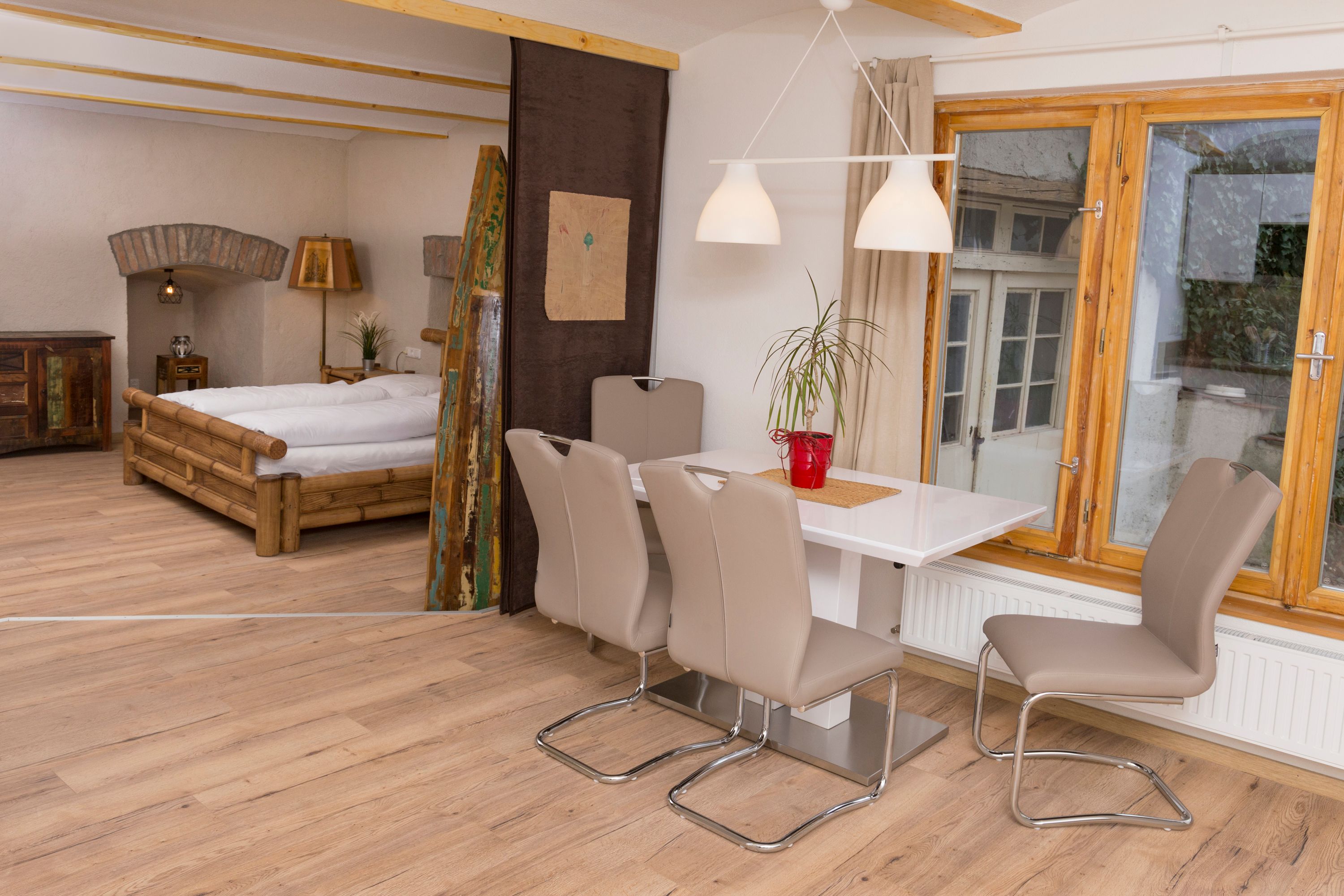 Pohľad do interiéru prázdninového bytu s jedálenským stolom, stoličkami, posteľou a oknom.