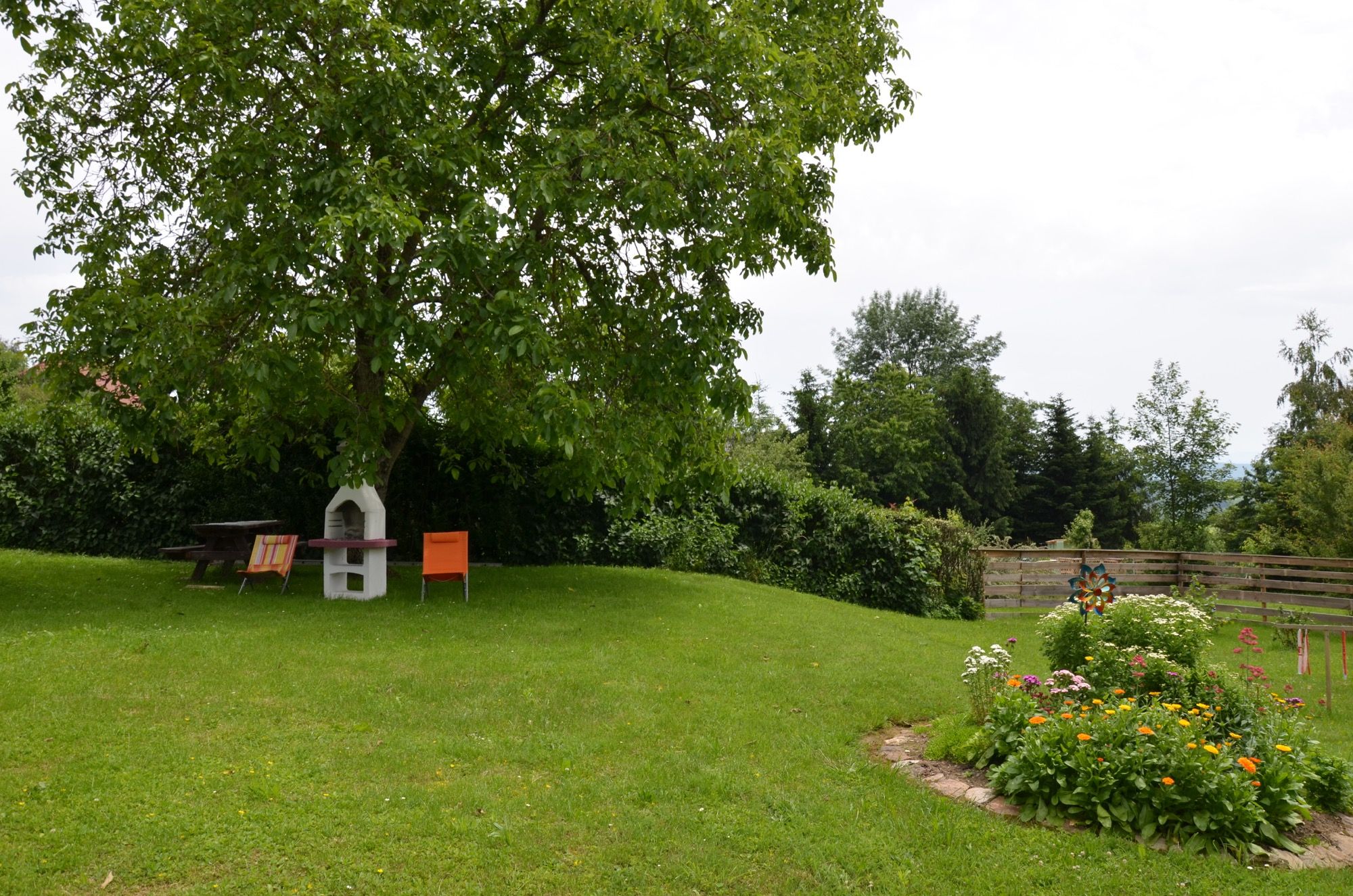 Zelená záhrada so stromom, záhradným nábytkom a kvetinovým záhonom.