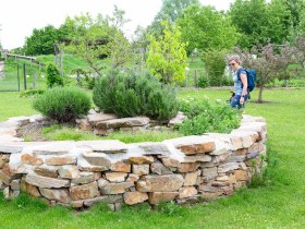 Žena stoj&iacute; vedľa bylinkov&eacute;ho slim&aacute;ka v parku alchymistov, obklopen&aacute; zelenou veget&aacute;ciou.