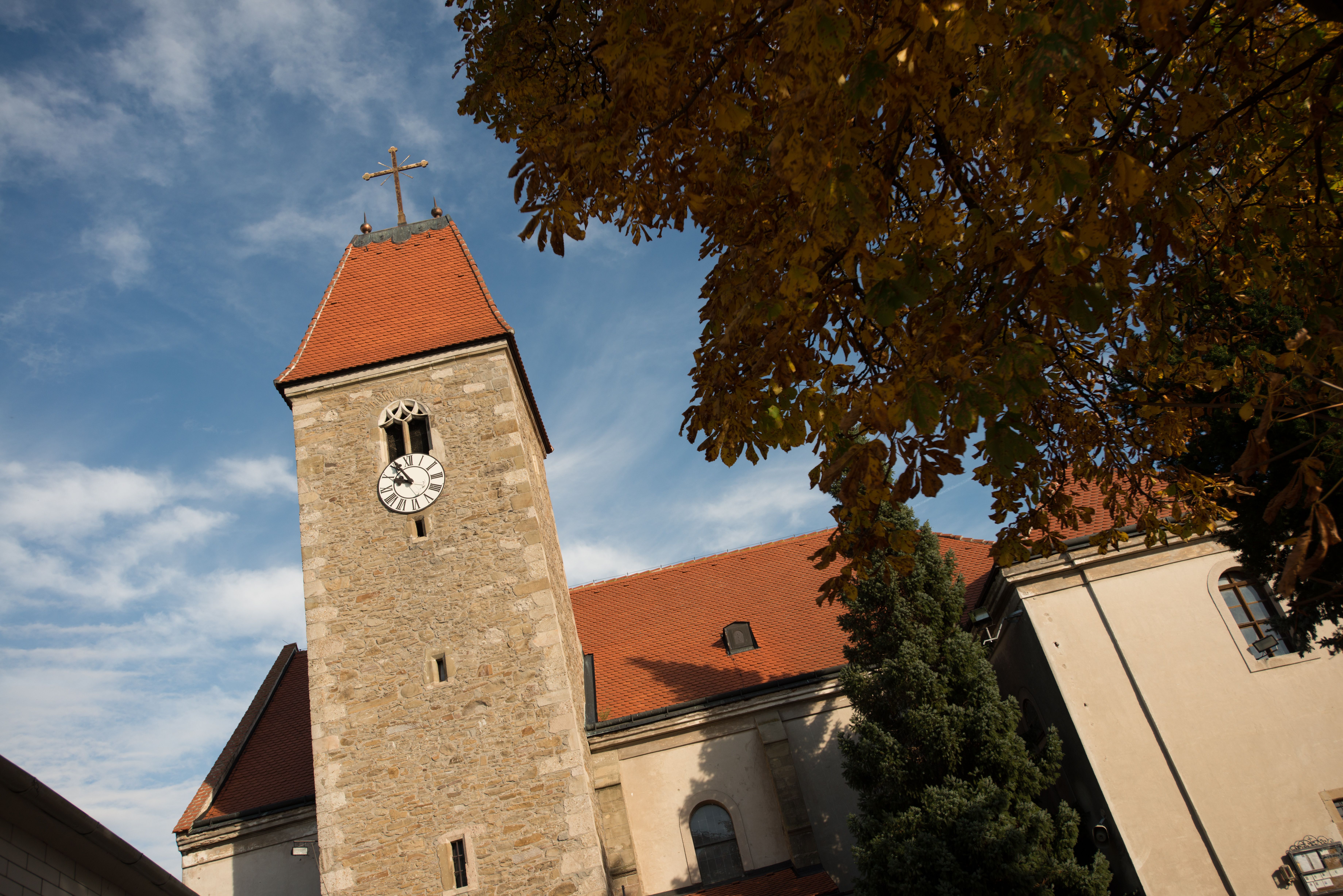 Veža kostola vo Weißenkirchene s hodinami a červenou strechou, obklopená jesenným lístím a modrou oblohou.