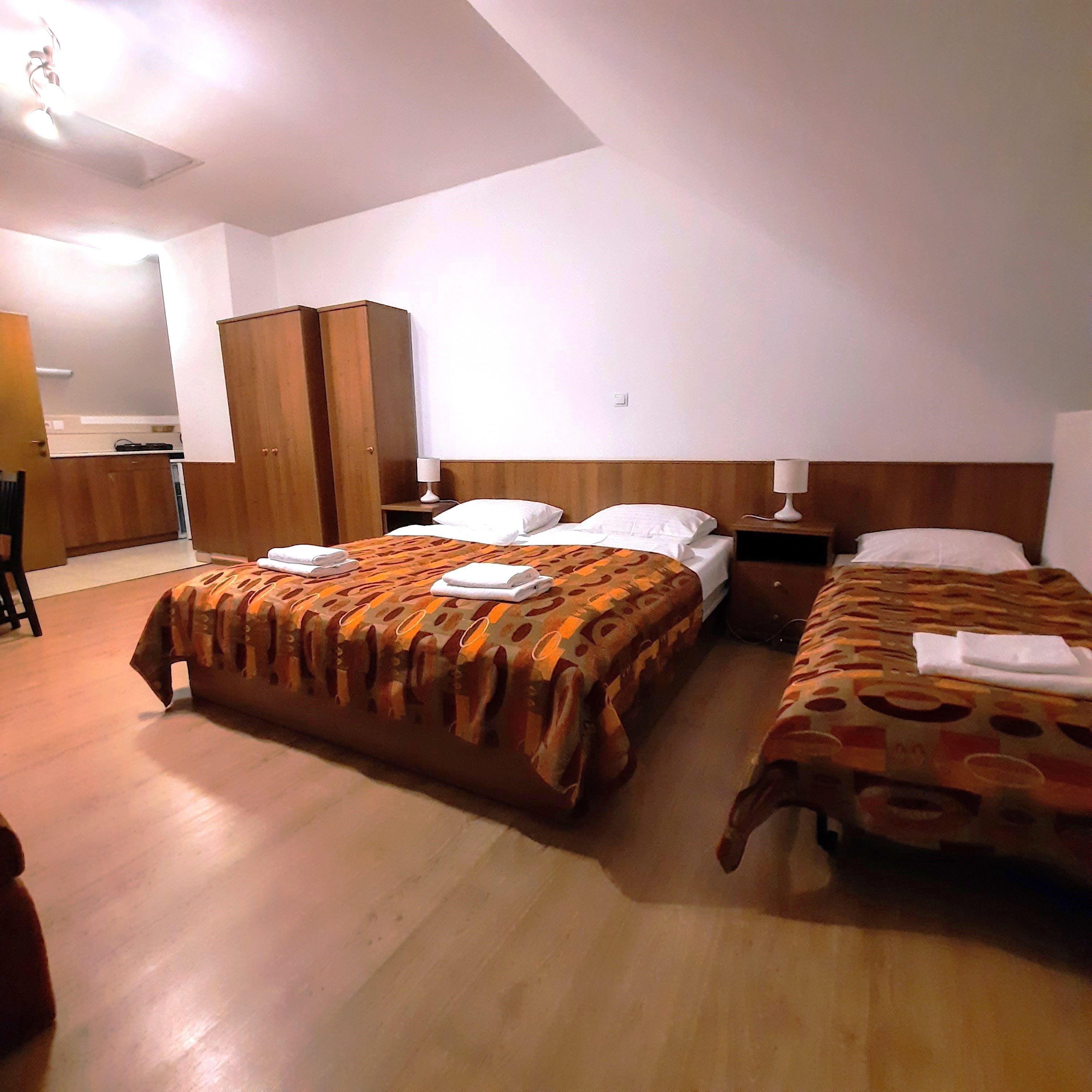 Trojlôžková izba s dvoma samostatnými posteľami a manželskou posteľou, všetky so vzorovanými prikrývkami. K dispozícii je aj šatníková skriňa a nočné stolíky.