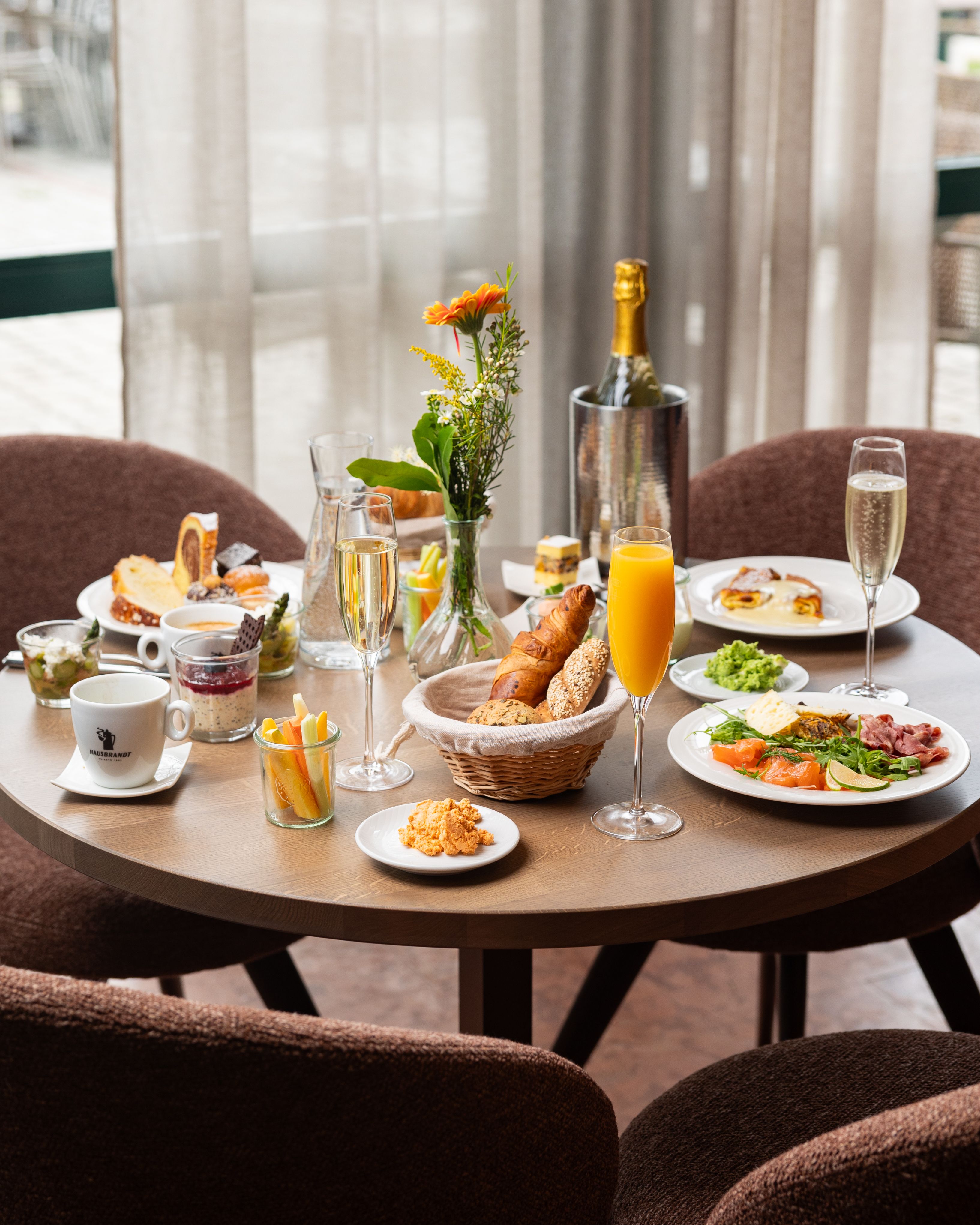 Položený raňajkový stôl s rôznymi jedlami, nápojmi a kvetmi.