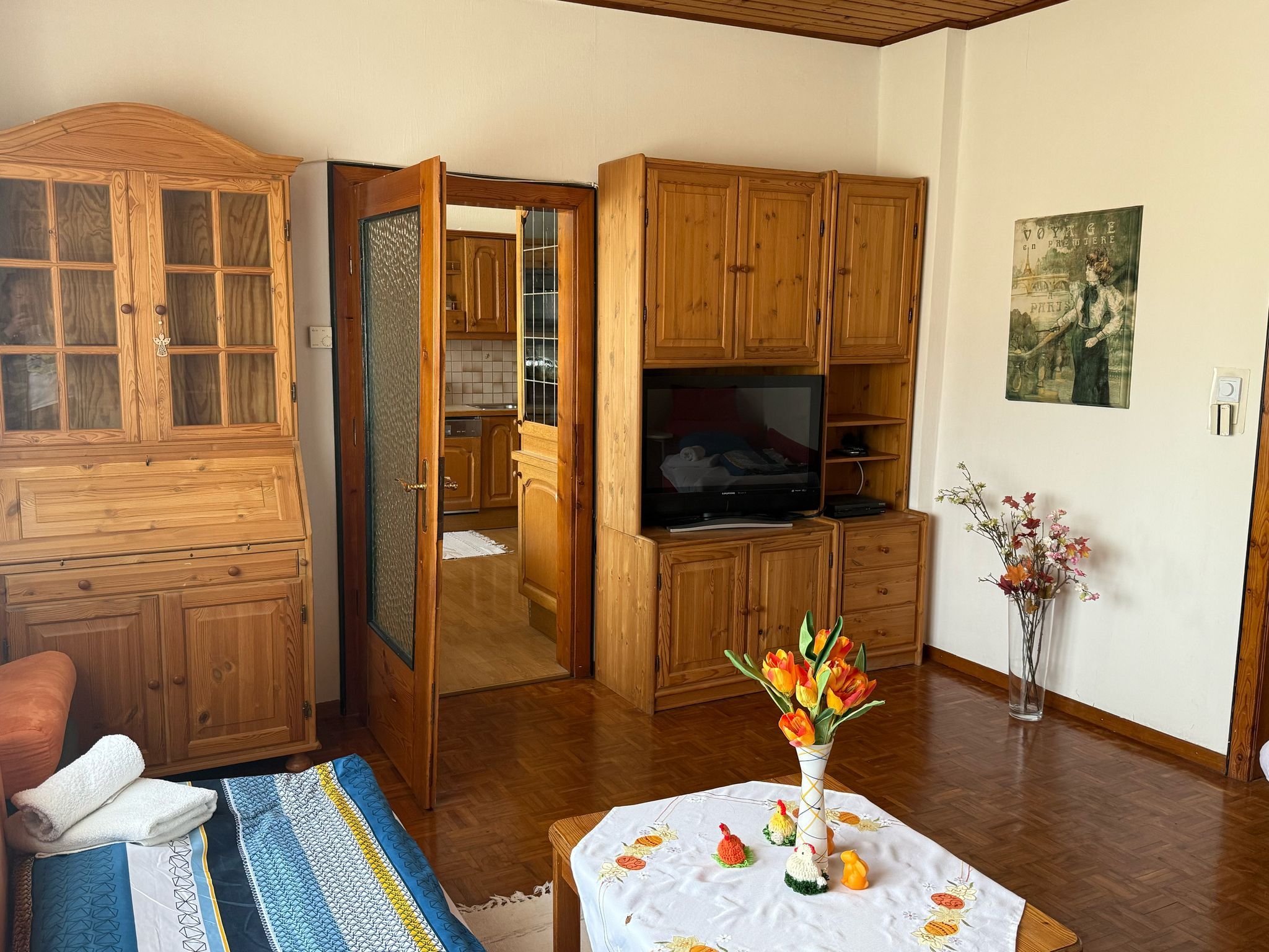 Obývacia izba s dreveným nábytkom, stolom s kvetmi a televízorom.