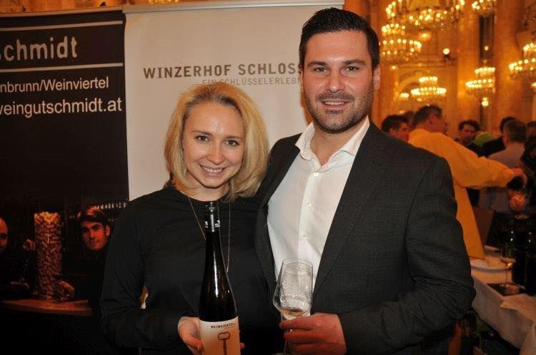 Pár drží fľašu vína a pohár s vínom pred transparentom s nápisom "Winzerhof Schlosser".