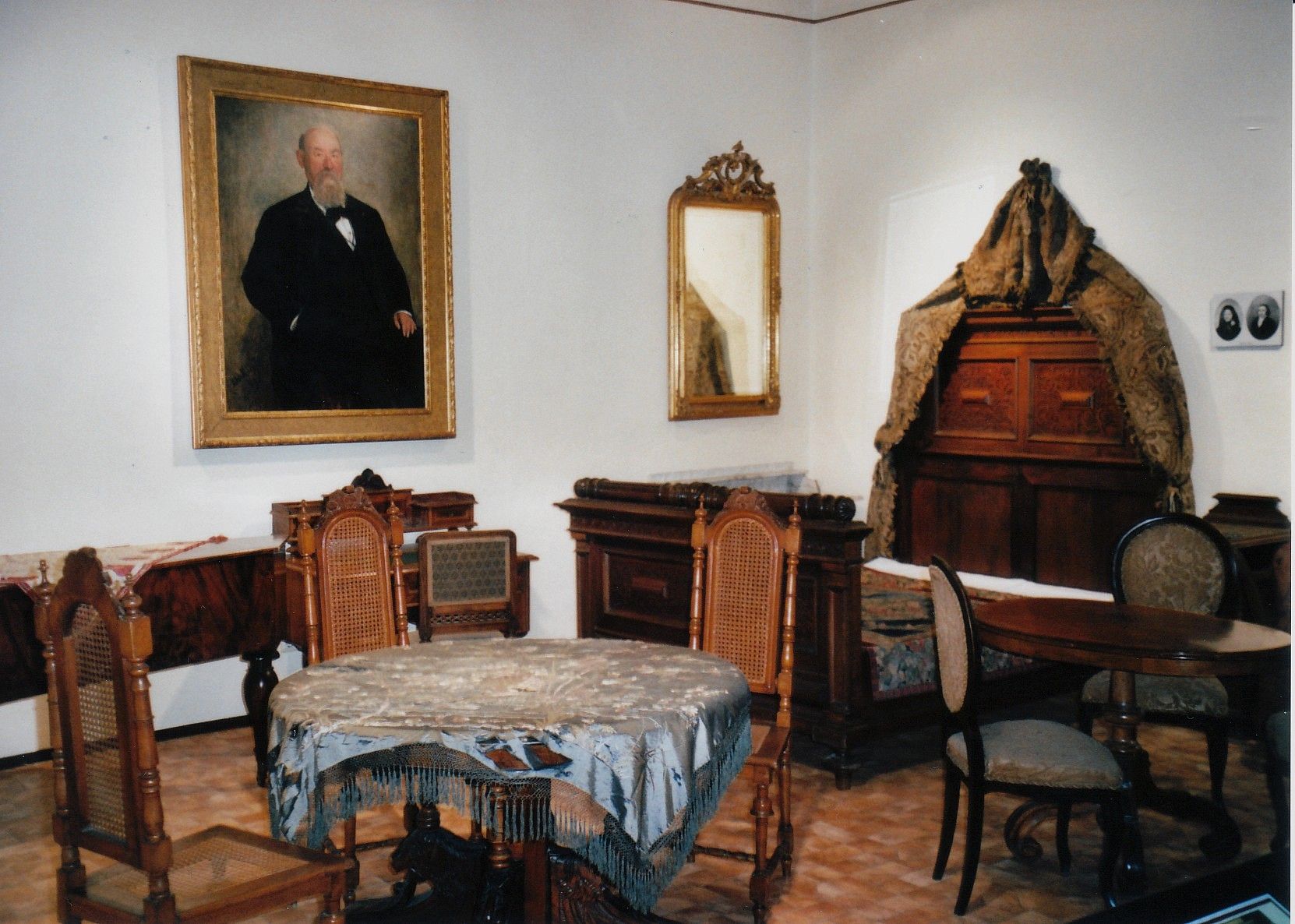 Historická izba so starožitným nábytkom a obrazom muža na stene.