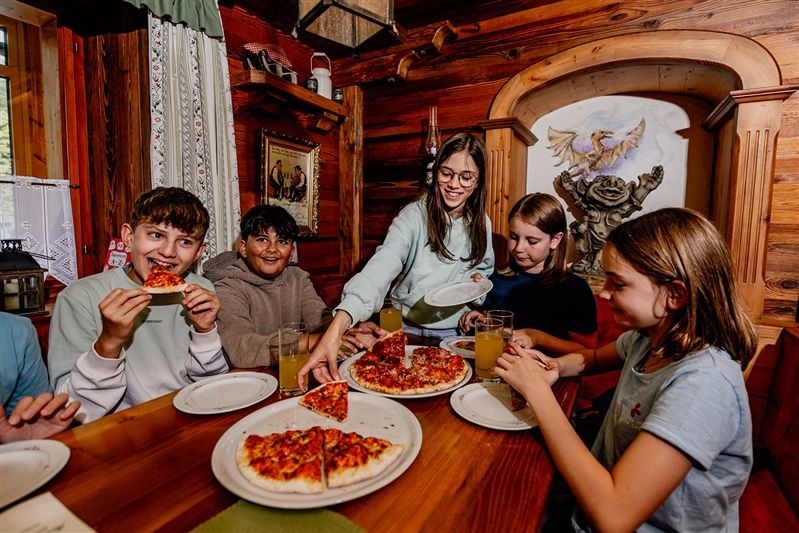 Deti jedia pizzu v rustikálnej miestnosti s drevenými stenami.