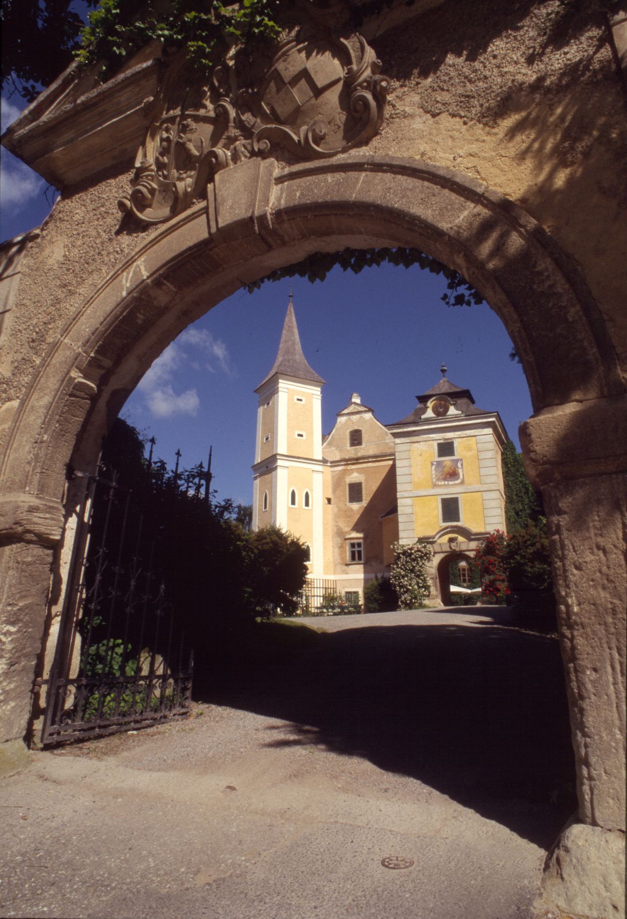 Historická budova s vežou videná cez kamenný oblúk.