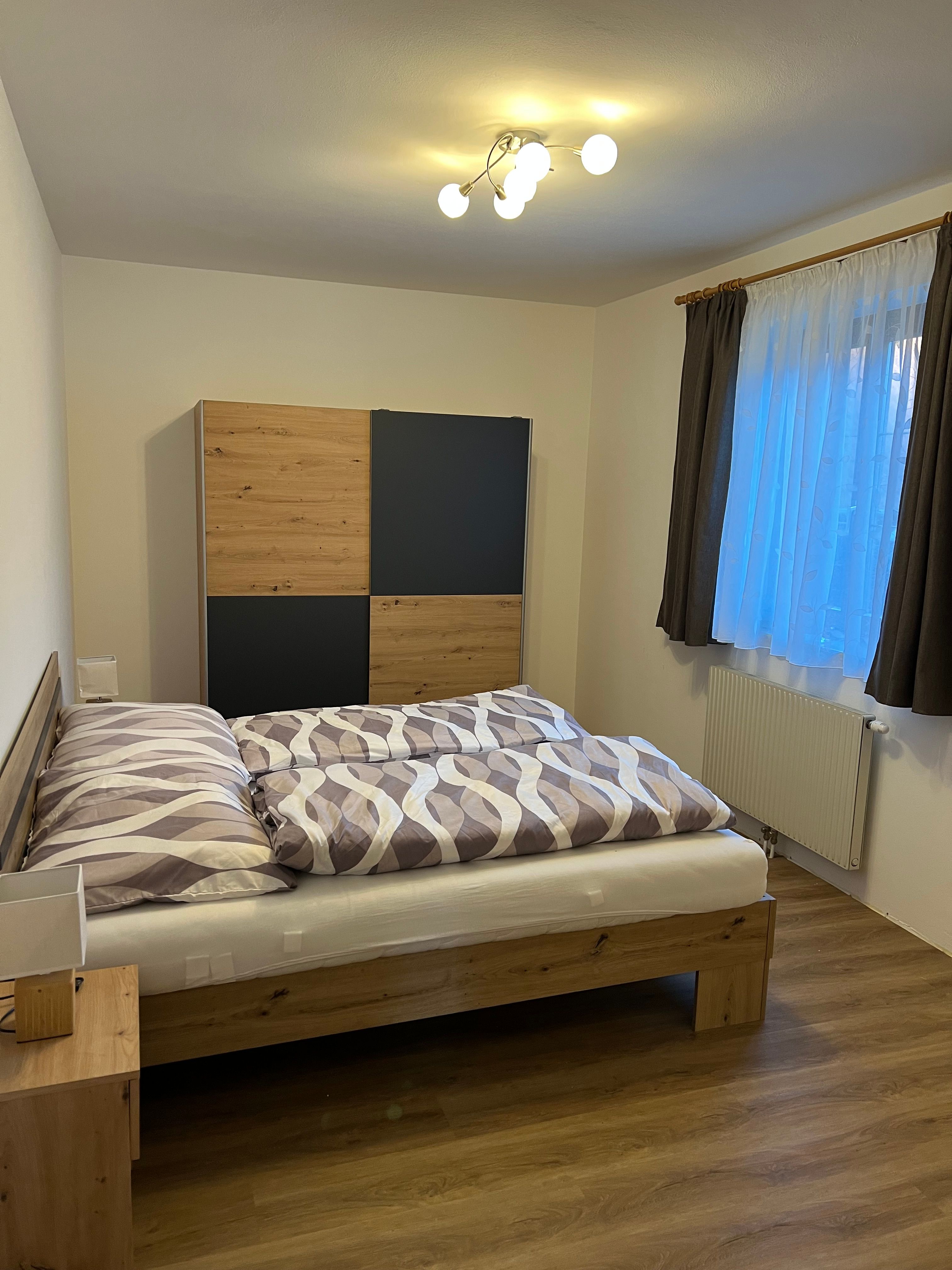 Útulná dvojlôžková izba s drevenou posteľou, šatníkovou skriňou a oknom so závesmi.