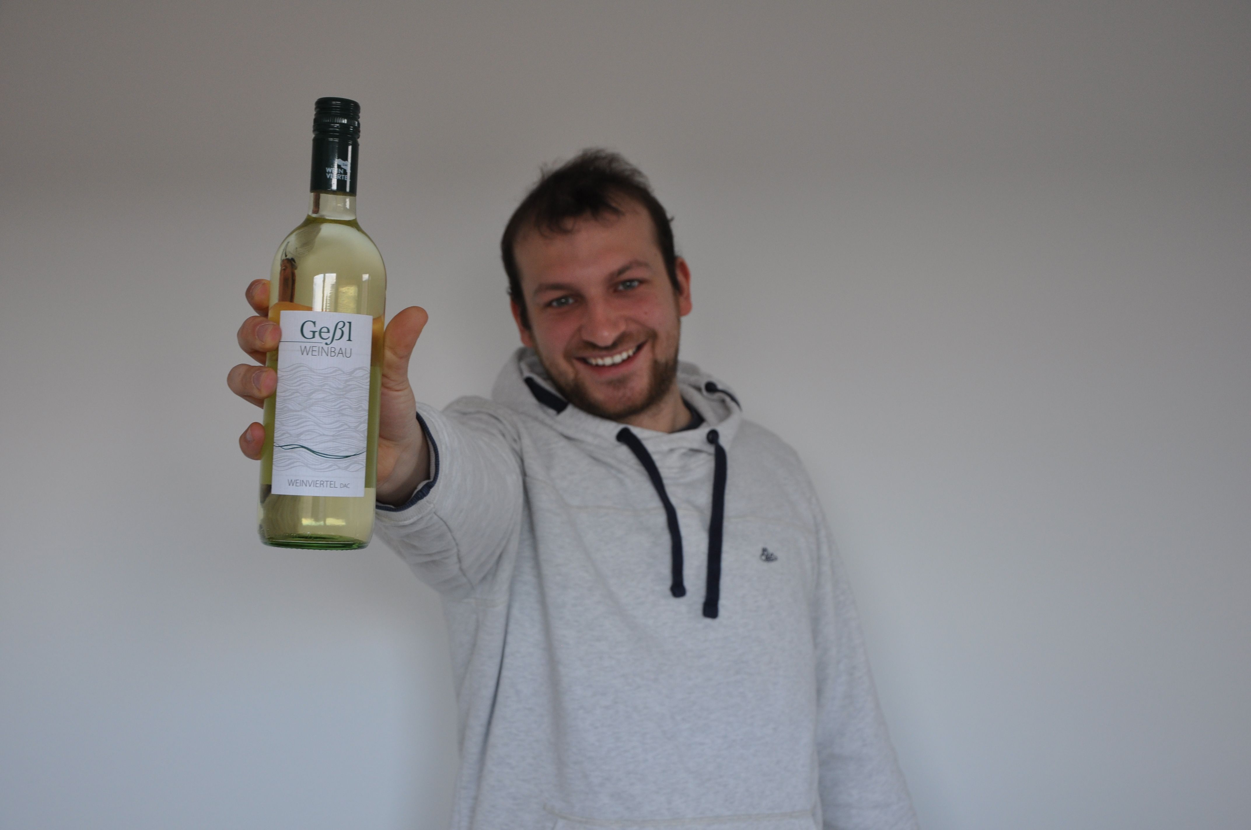 Muž drží pred kamerou fľašu bieleho vína Geßl Weinbau.