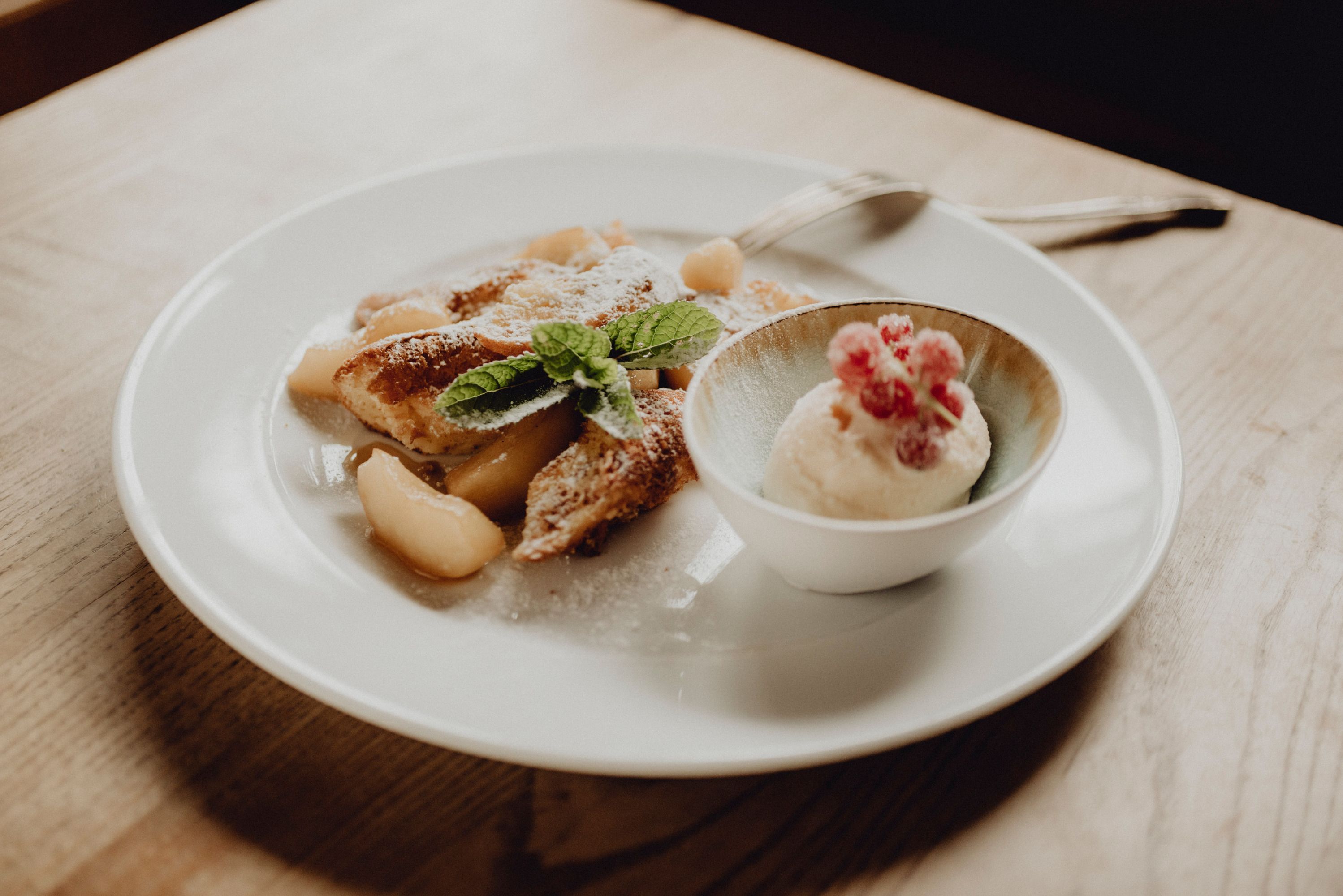 Tanier jablkových palaciniek a miska tvarohovo-rumovej zmrzliny, ozdobená lístkami mäty a červenými bobuľami.