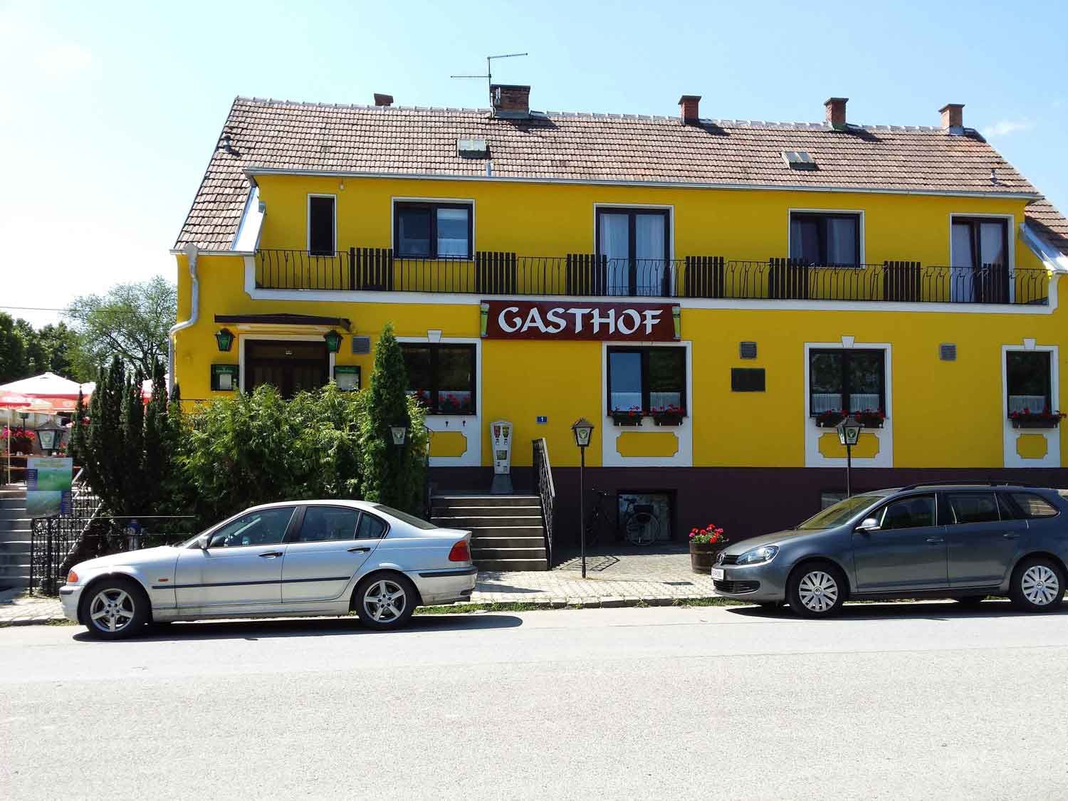 Žltá budova s nápisom "Gasthof", pred ňou zaparkované autá.