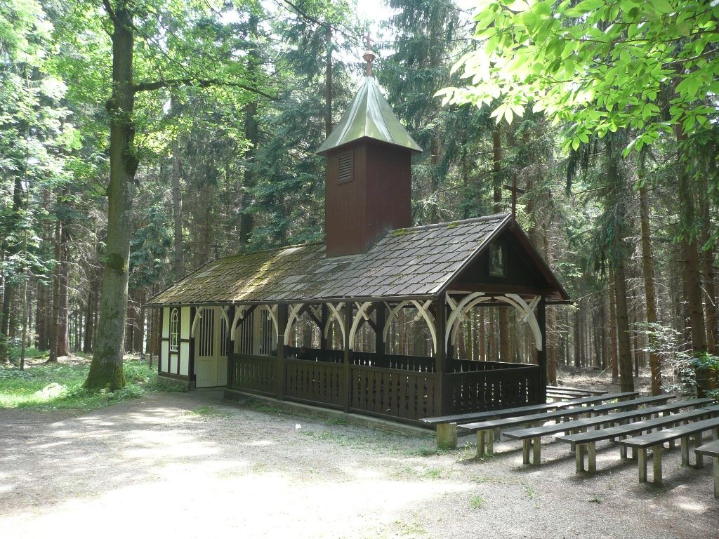 Malá kaplnka v lese s drevenými lavičkami vonku.
