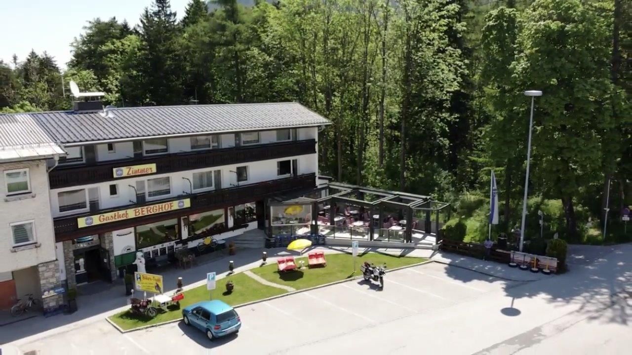 Vonkajší pohľad na penzión Gasthof Berghof s terasou a parkoviskom, obklopený stromami.