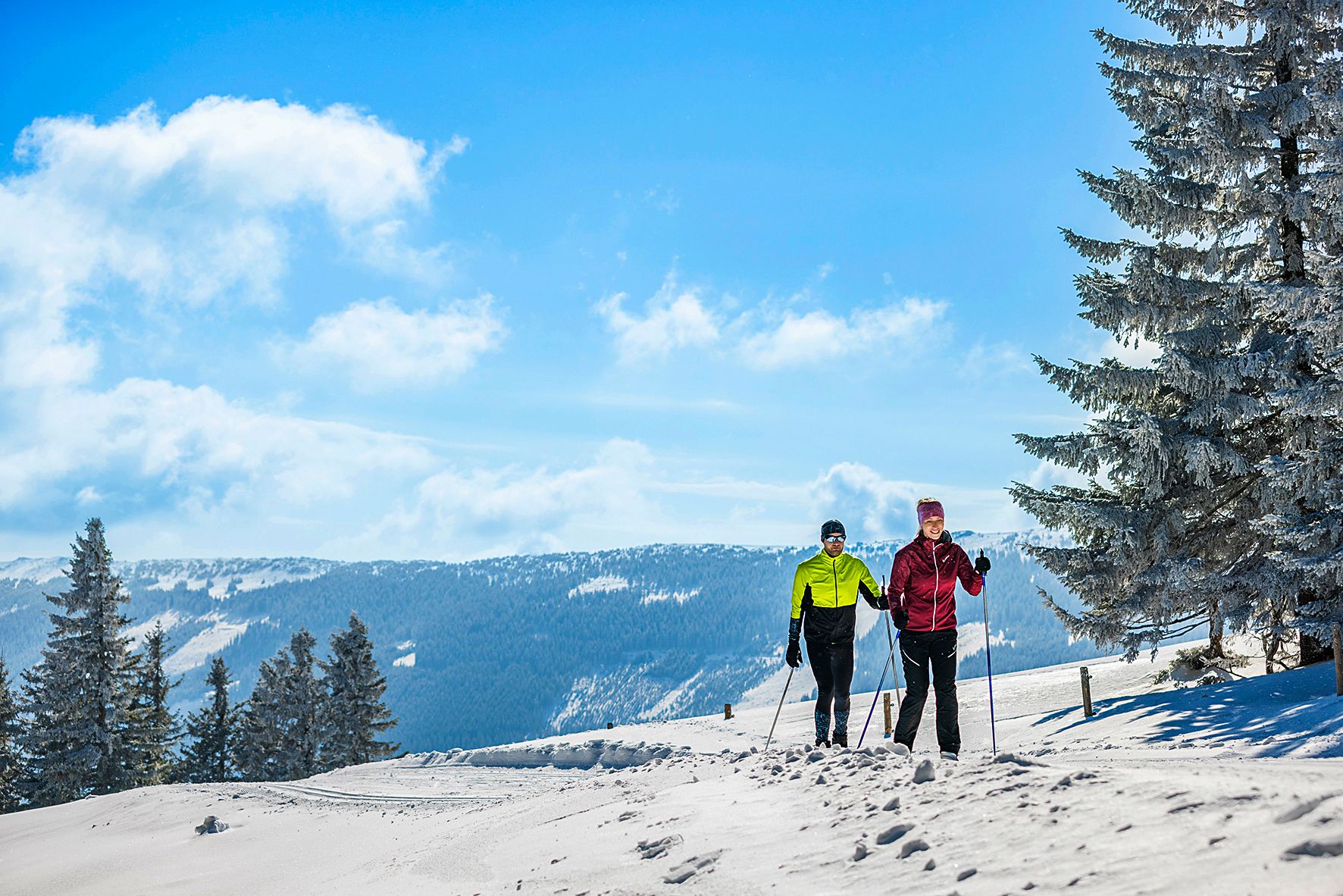 Dvaja ľudia na bežkách na zasneženej trase v zimnej horskej krajine.