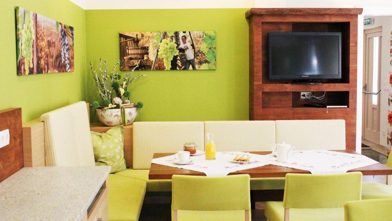 Útulná jedáleň so zelenými stenami, dreveným nábytkom a TV.