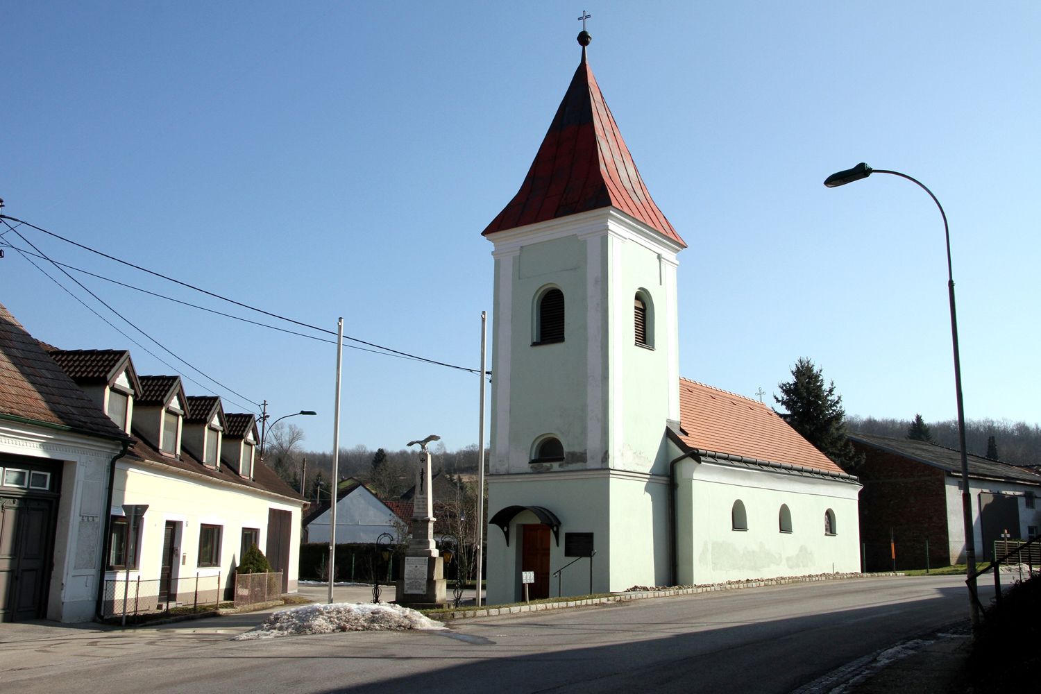 Kostol s červenou strechou a vežou v dedine pod jasnou oblohou.