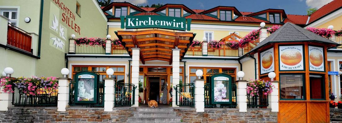 Vchod do reštaurácie Kirchenwirt s kvetmi a nápismi.