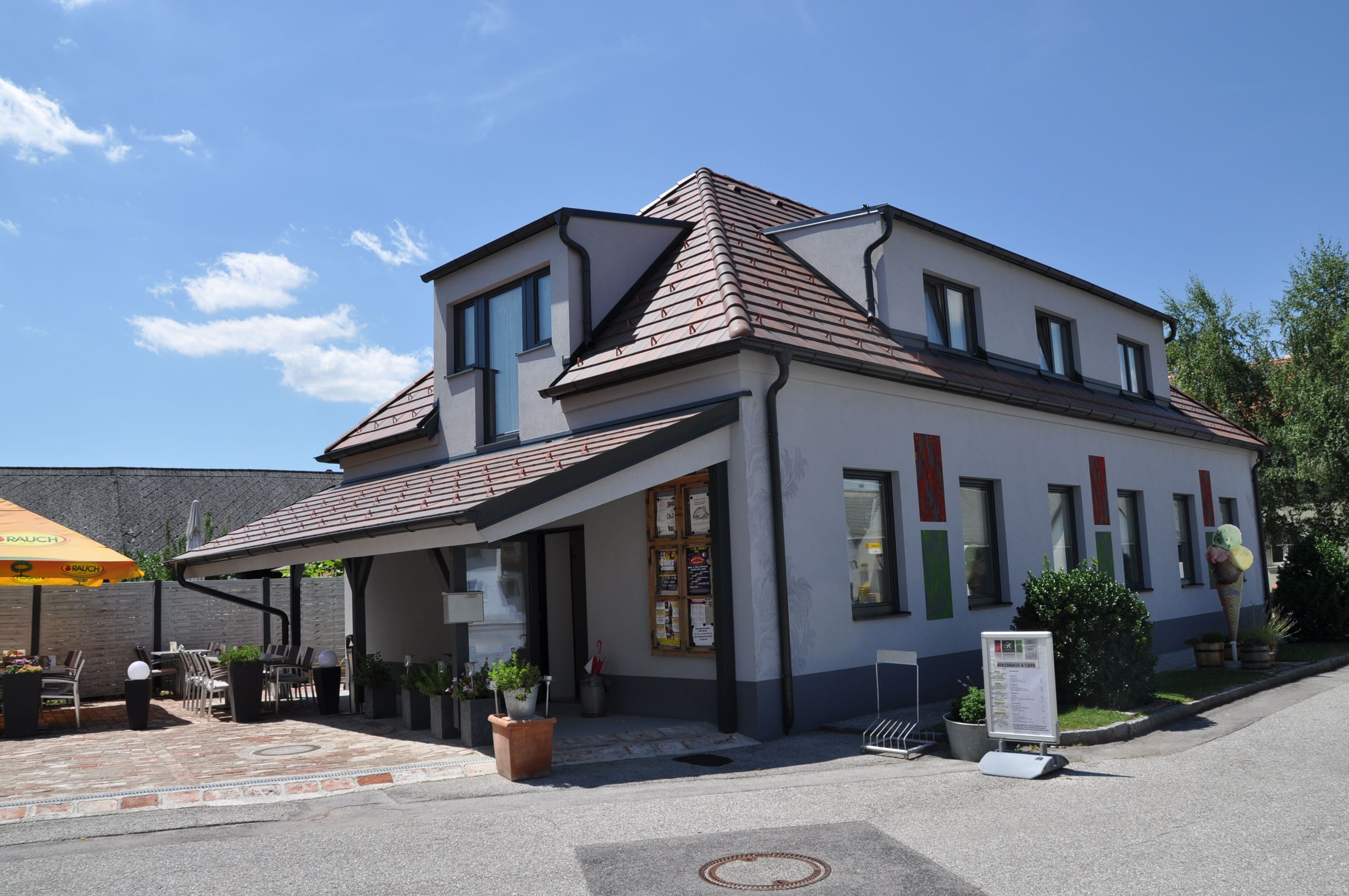 Moderná budova s terasou a slnečníkom počas slnečného dňa.