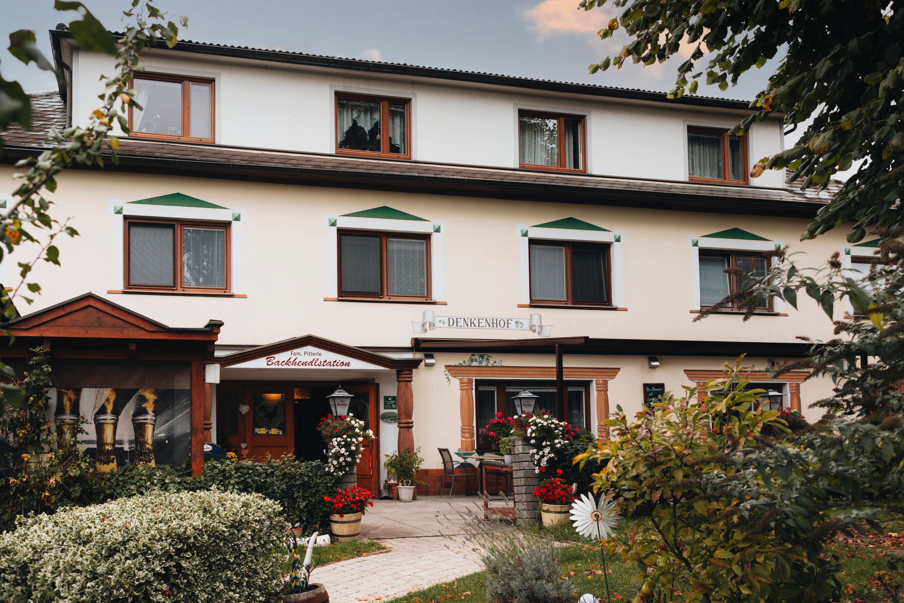 Tradičný hostinec s kvetmi a stromami v popredí.