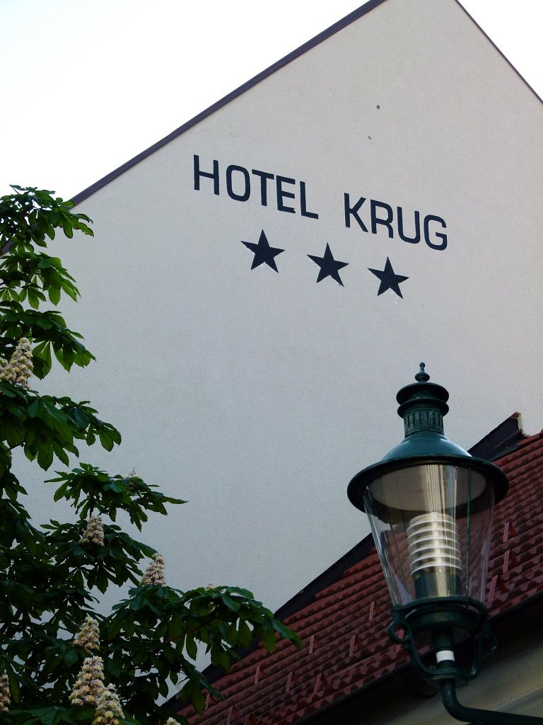 Fasáda hotela Krug s tromi hviezdami, stromom a pouličnou lampou.