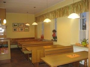 Pohľad do interiéru útulnej kaviarne s drevenými stolmi a lavicami, zdobenej obrazmi a rastlinami.