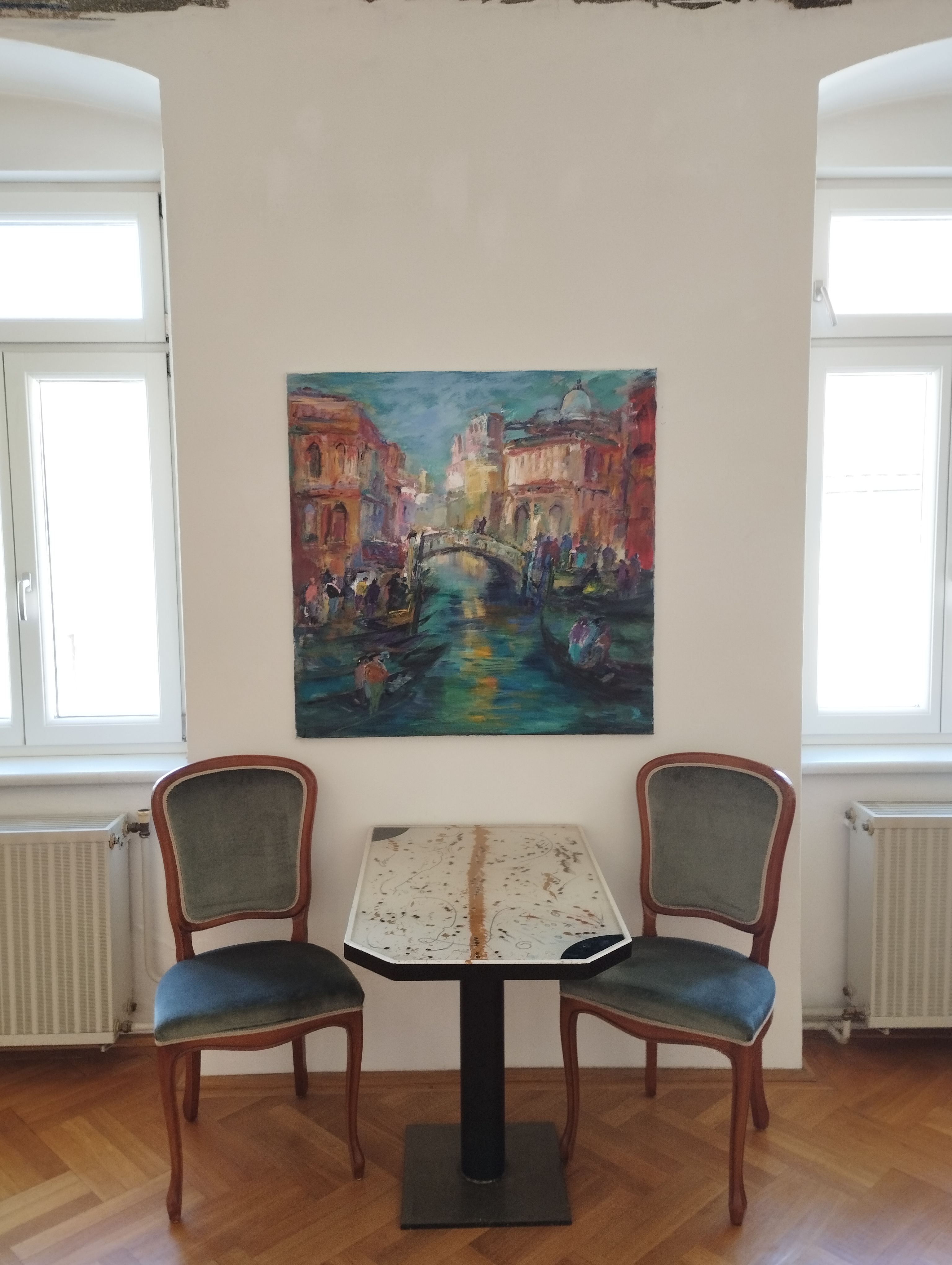 Dve stoličky a stôl pred obrazom na bielej stene.
