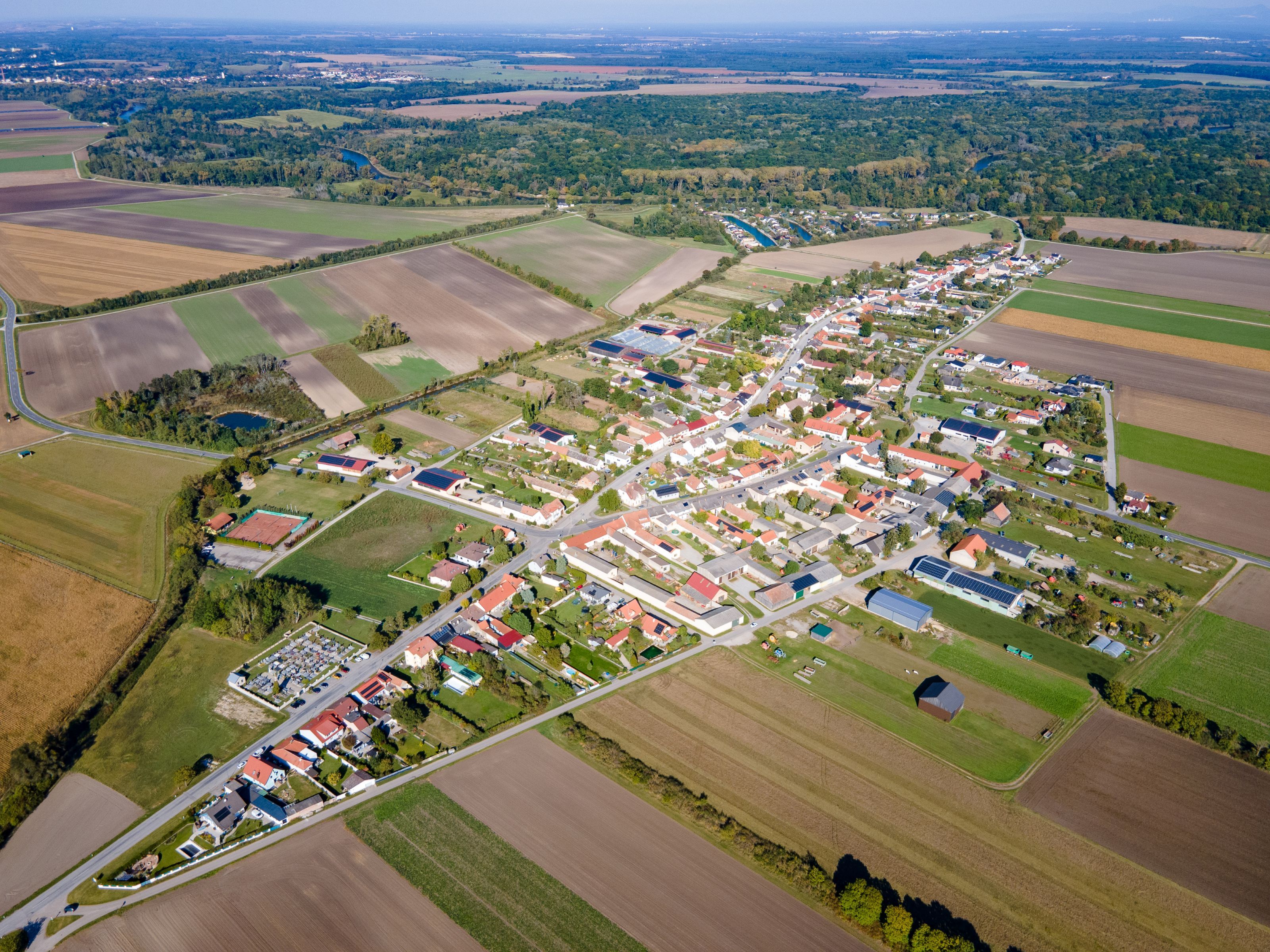 Letecký pohľad na obec Weiden an der March s poľami, obytnými domami a tokom rieky v pozadí.