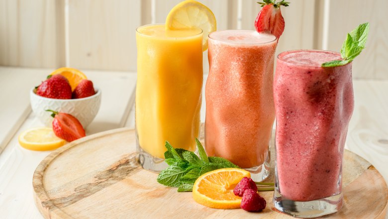 Tri smoothies v poh&aacute;roch na drevenej doske, zdoben&eacute; ovoc&iacute;m a m&auml;tou.