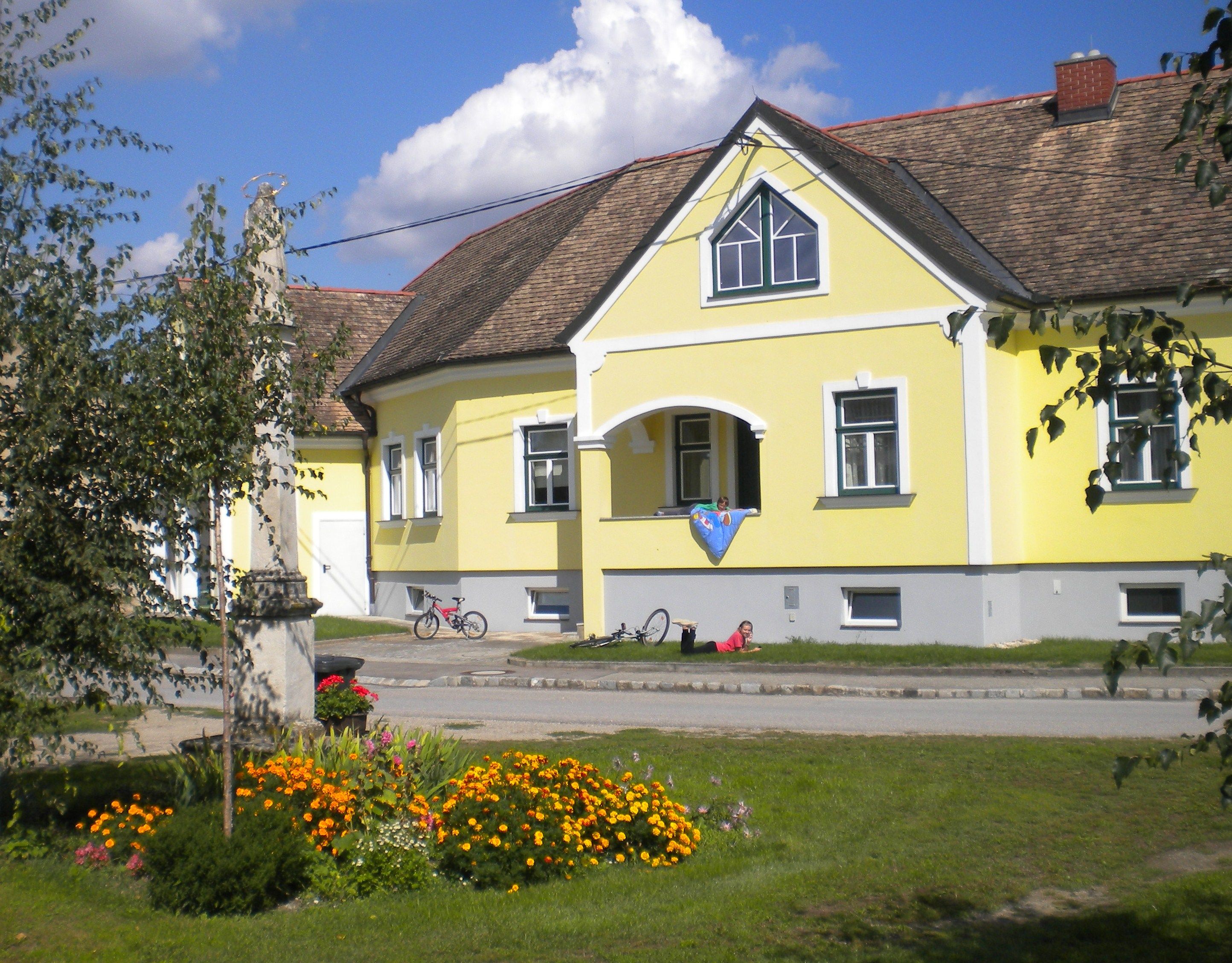 Žltý penzión s kvetinovým záhonom a bicyklami pred domom.
