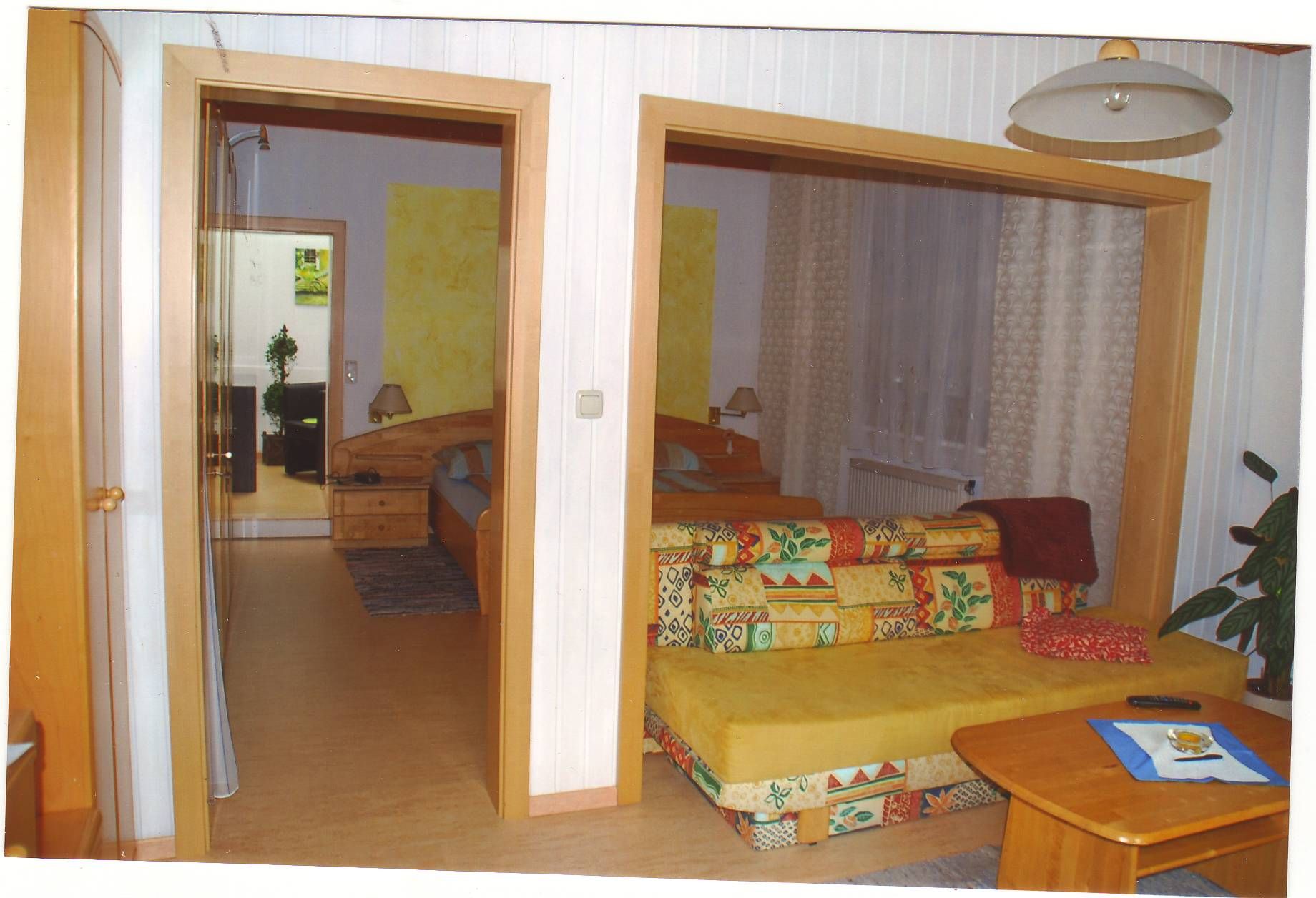 Útulná izba pre hostí s farebnou pohovkou, dreveným stolom a výhľadom na spálňu s manželskou posteľou.